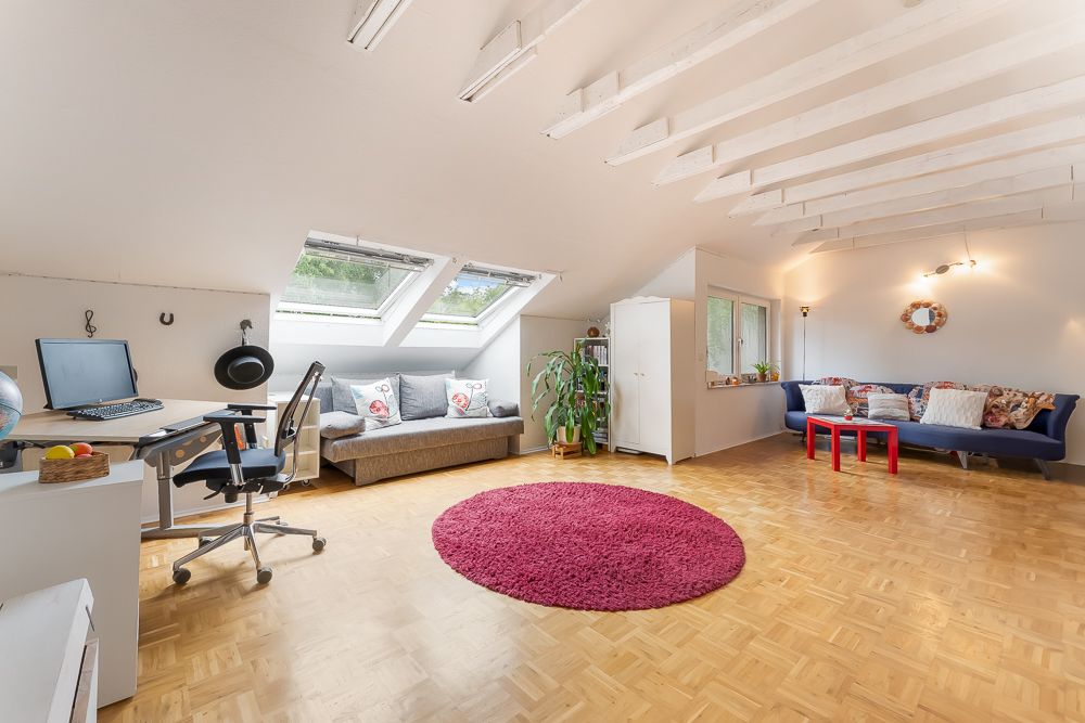 Helles Dachzimmer mit Schreibtisch, Sofa, blauem Sofa, Teppich und Pflanzen.