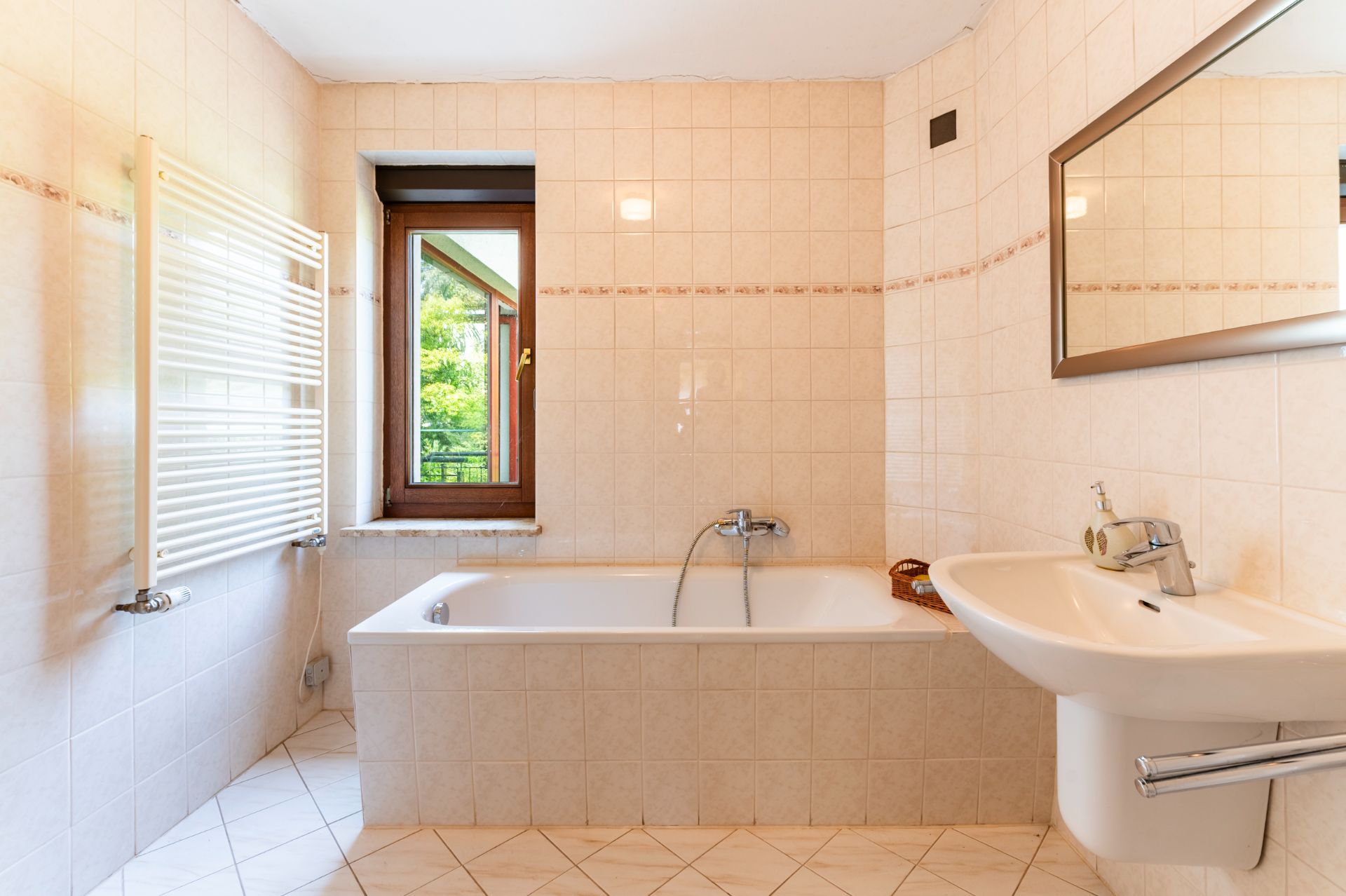 Helles Badezimmer mit Badewanne, Waschbecken, Fenster und Wandspiegel.