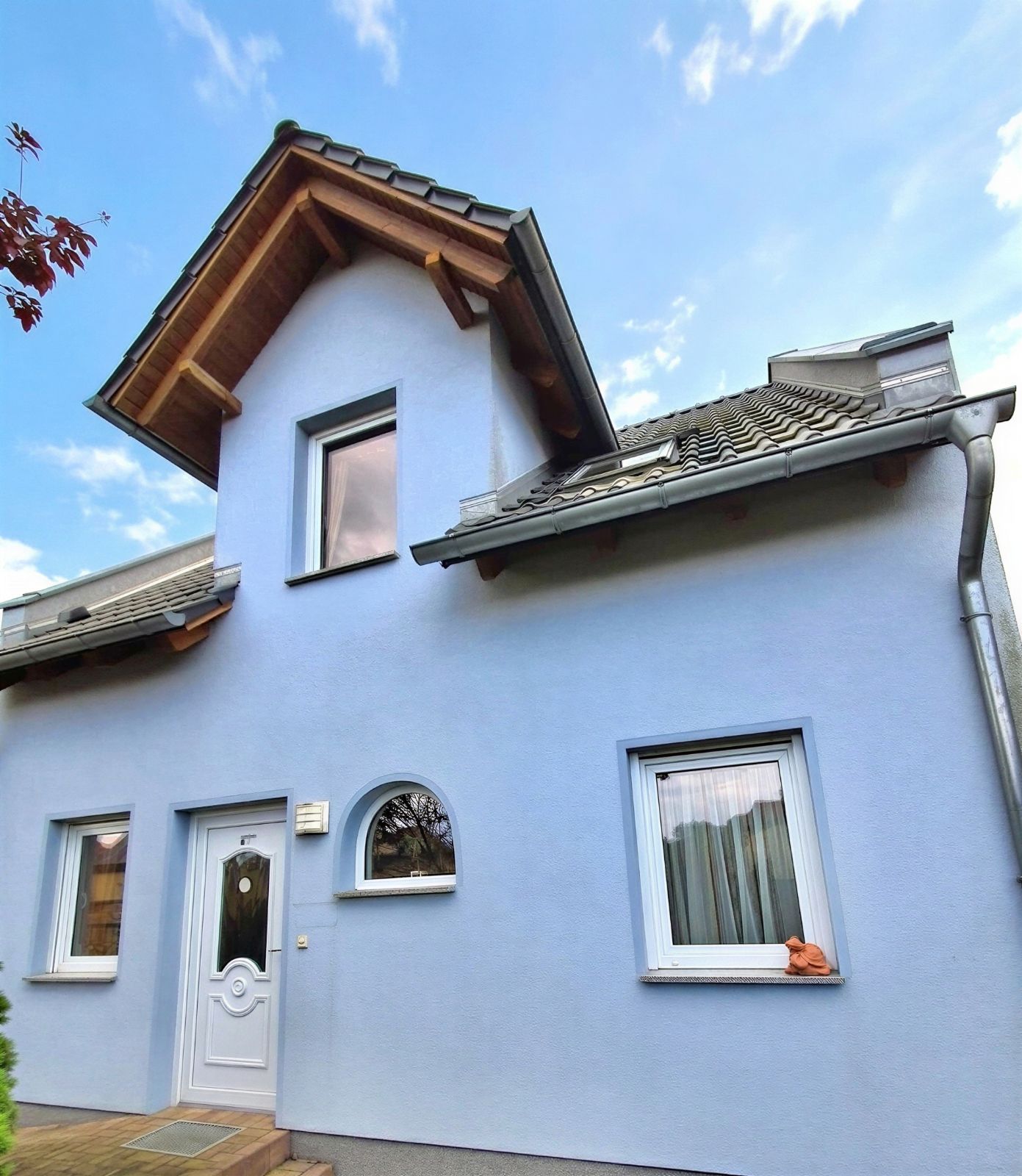 Hellblaues Wohnhaus mit Satteldach, drei Fenstern und weißer Haustür.