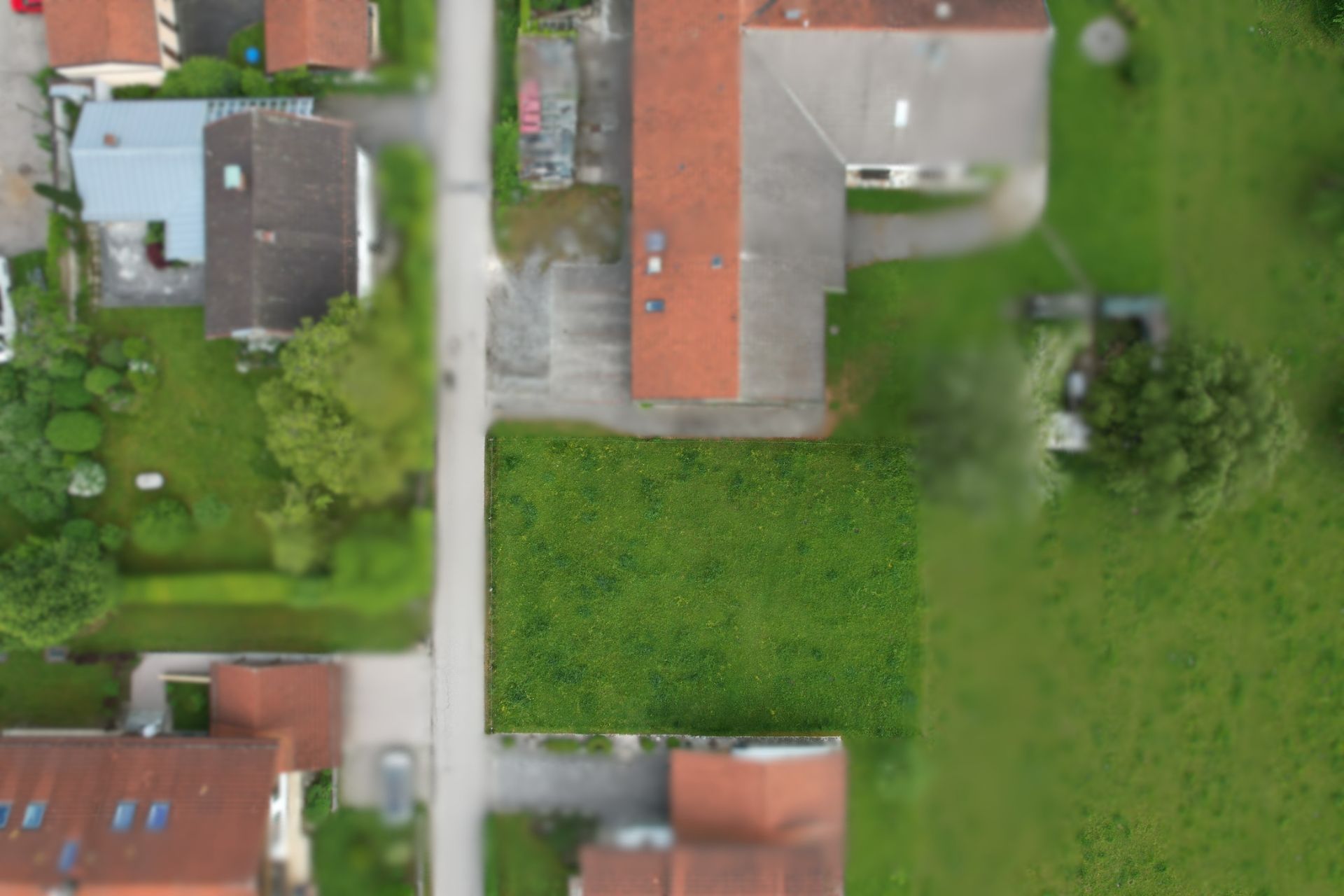Luftaufnahme eines rechteckigen, unbebauten Grundstücks zwischen Häusern und einer Straße.