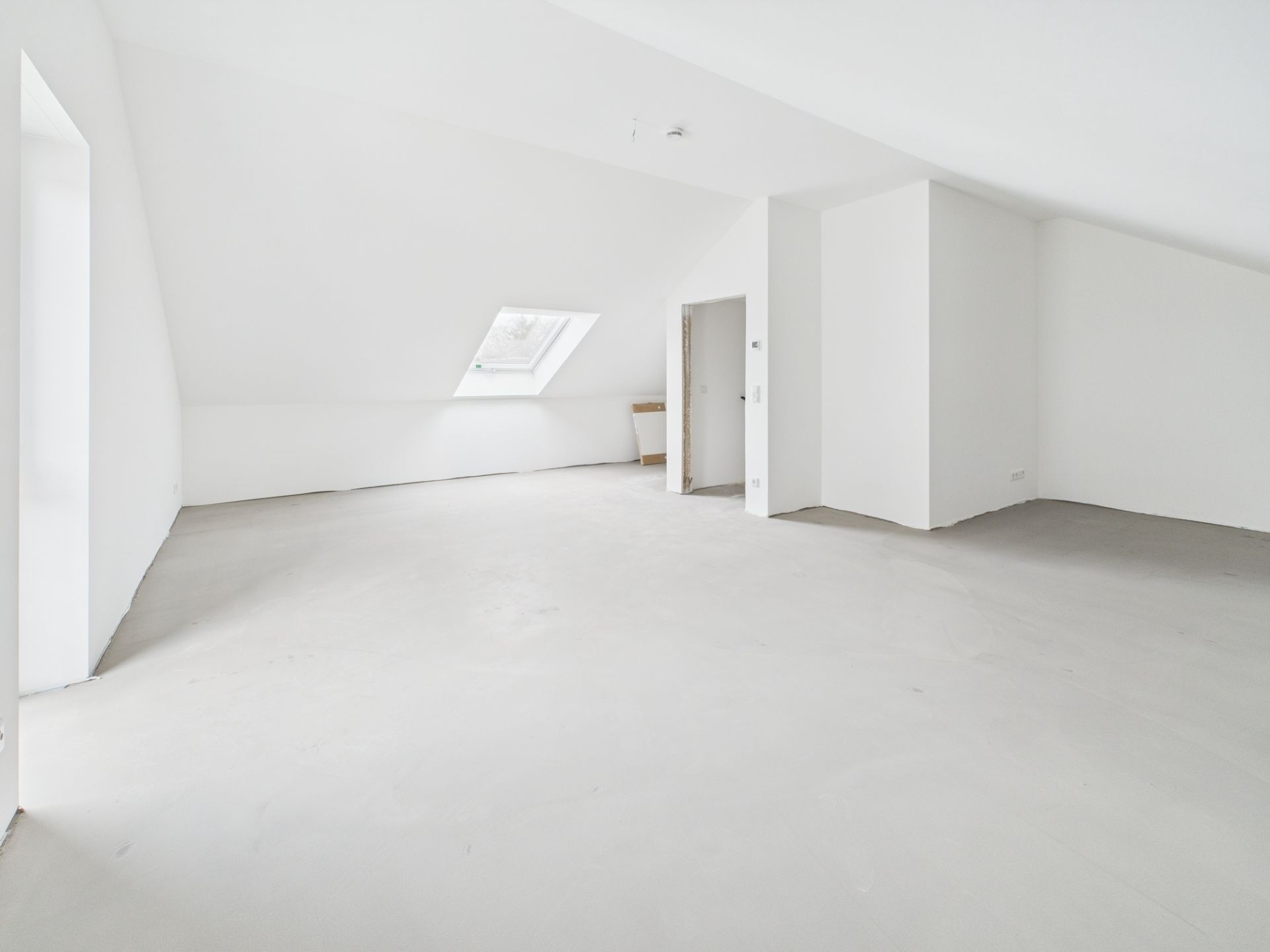 Heller, leerer Dachbodenraum mit schrägen Wänden und großem Dachfenster.
