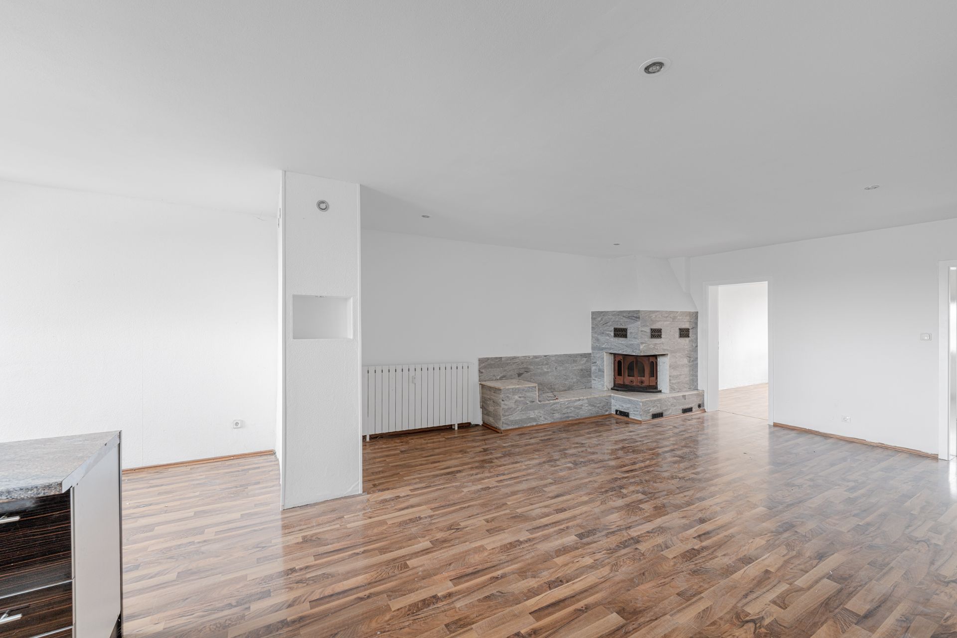 Leeres Wohnzimmer mit Holzboden, weißer Wand und Kamin in der Ecke.