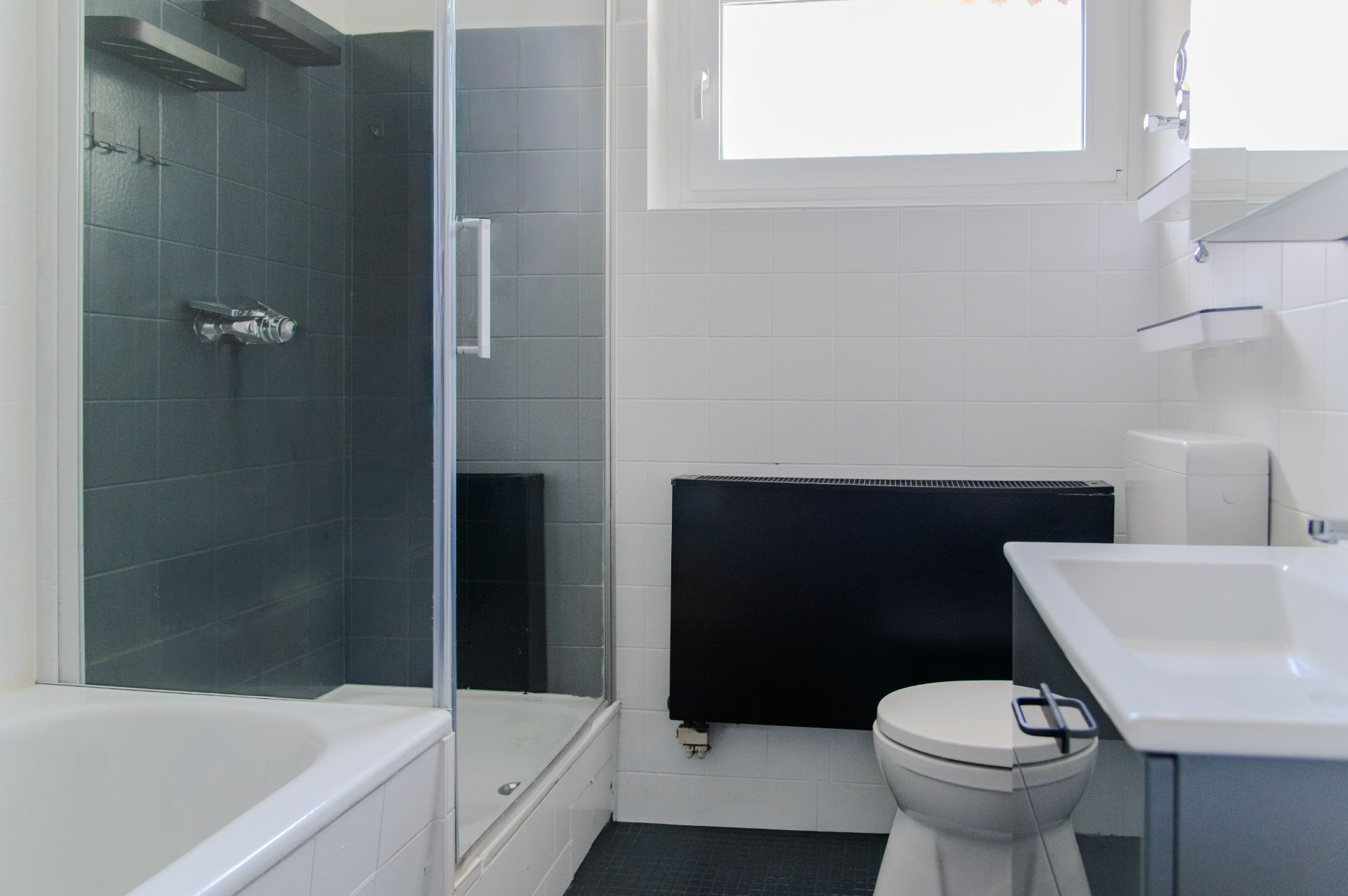 Helles Badezimmer mit Badewanne, Dusche, WC und Waschbecken unter dem Fenster.
