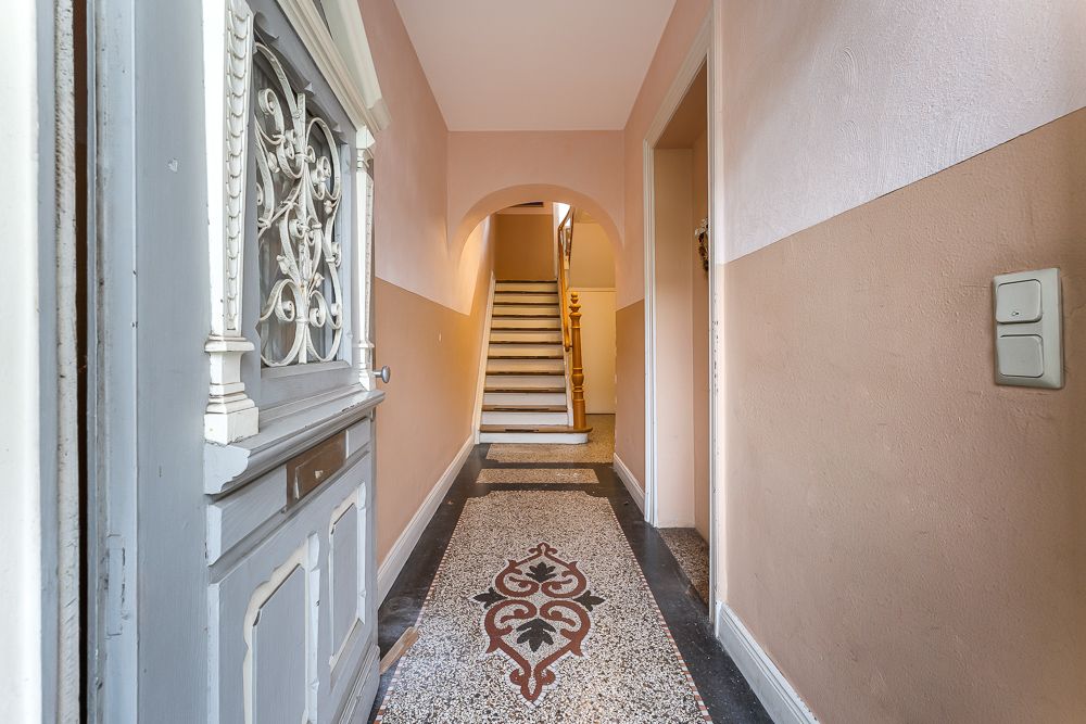 Eingangsflur mit verziertem Bodenmuster, offener Tür und Treppe im Hintergrund.