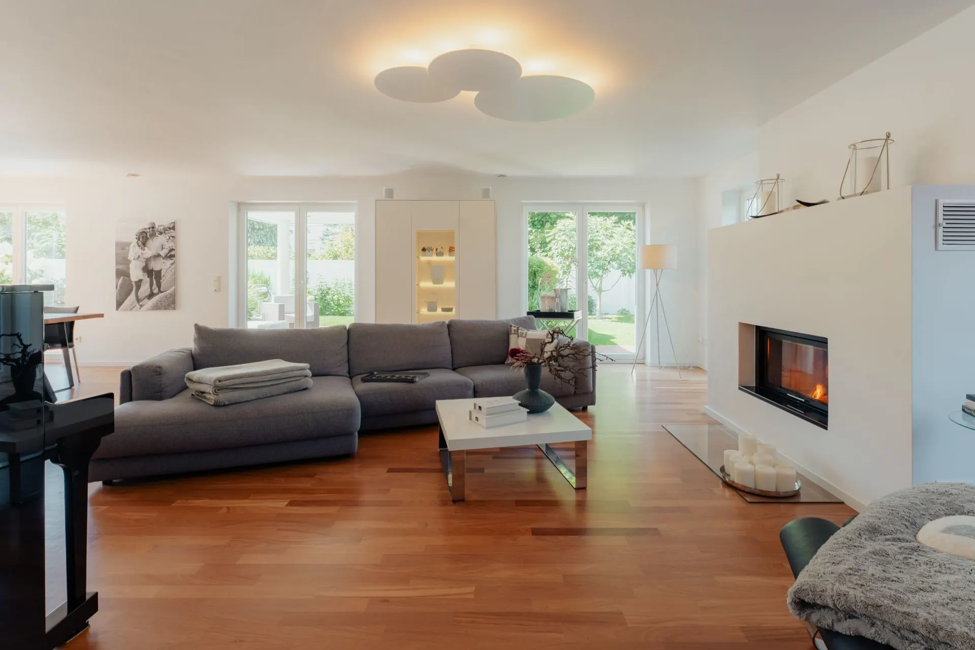 Modernes Wohnzimmer mit grauem Sofa, Kamin und großen Fenstern zum Garten.