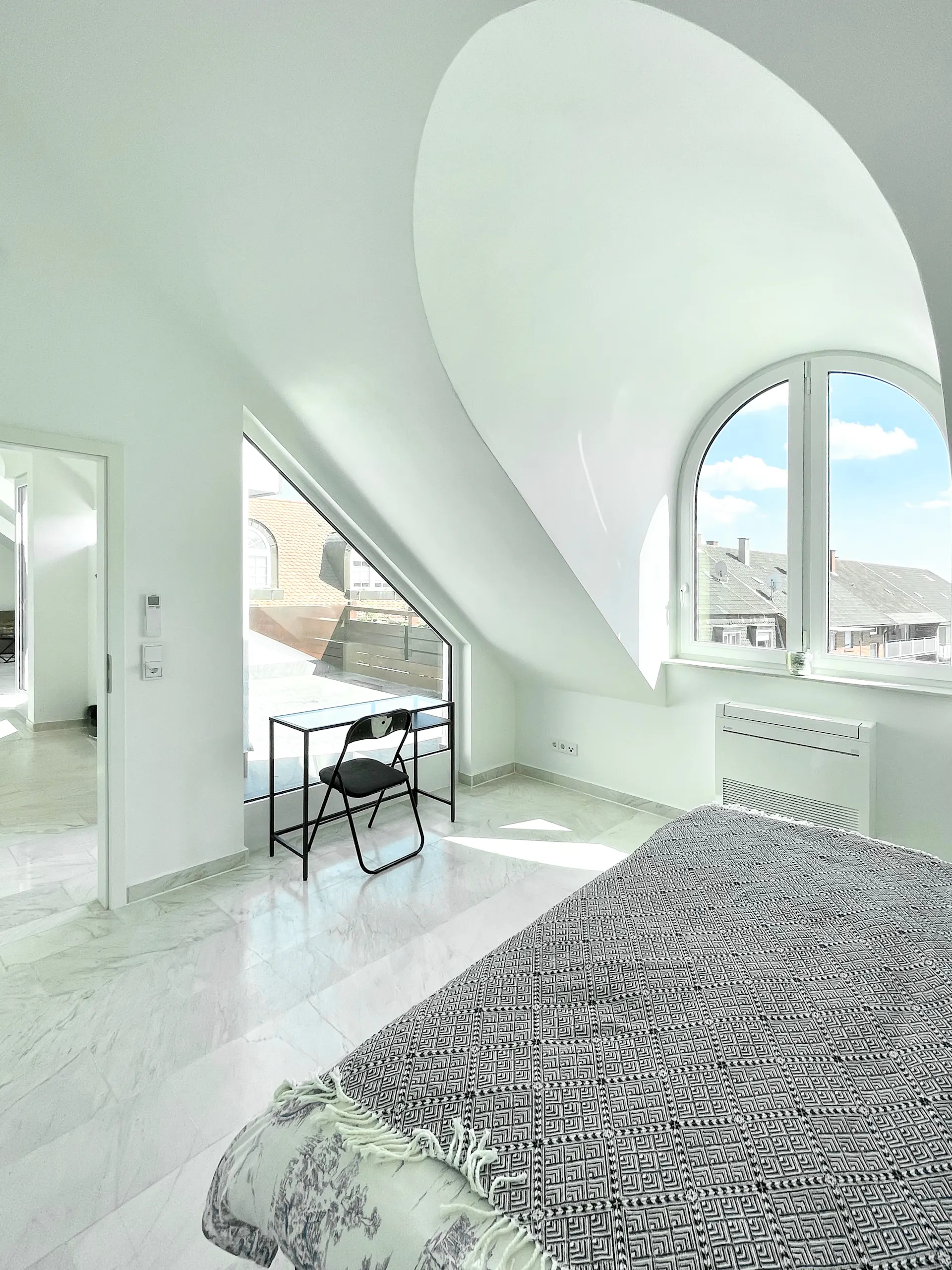 Helles Schlafzimmer mit großem Fenster, Bett, Schreibtisch und Stuhl im Dachgeschoss.