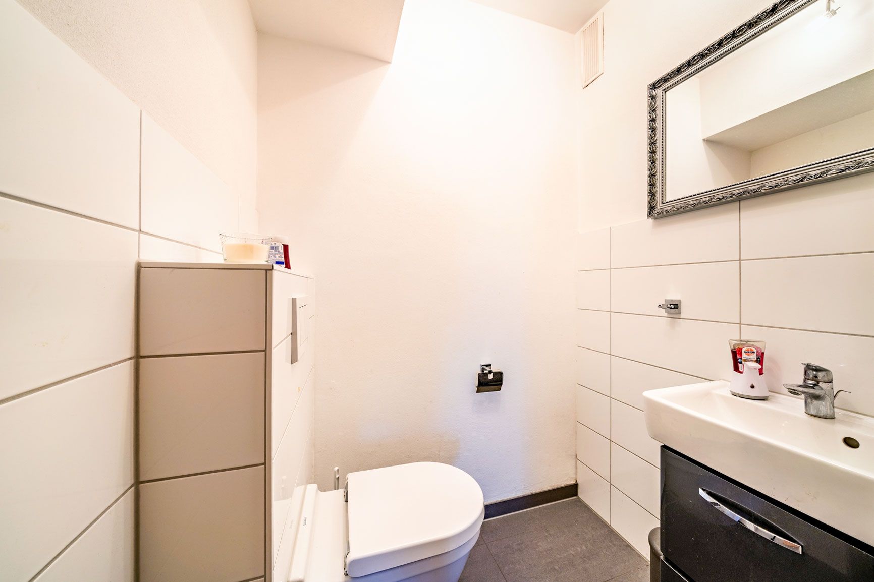 Kleines Badezimmer mit Toilette, Waschbecken und großem Spiegel an der Wand.