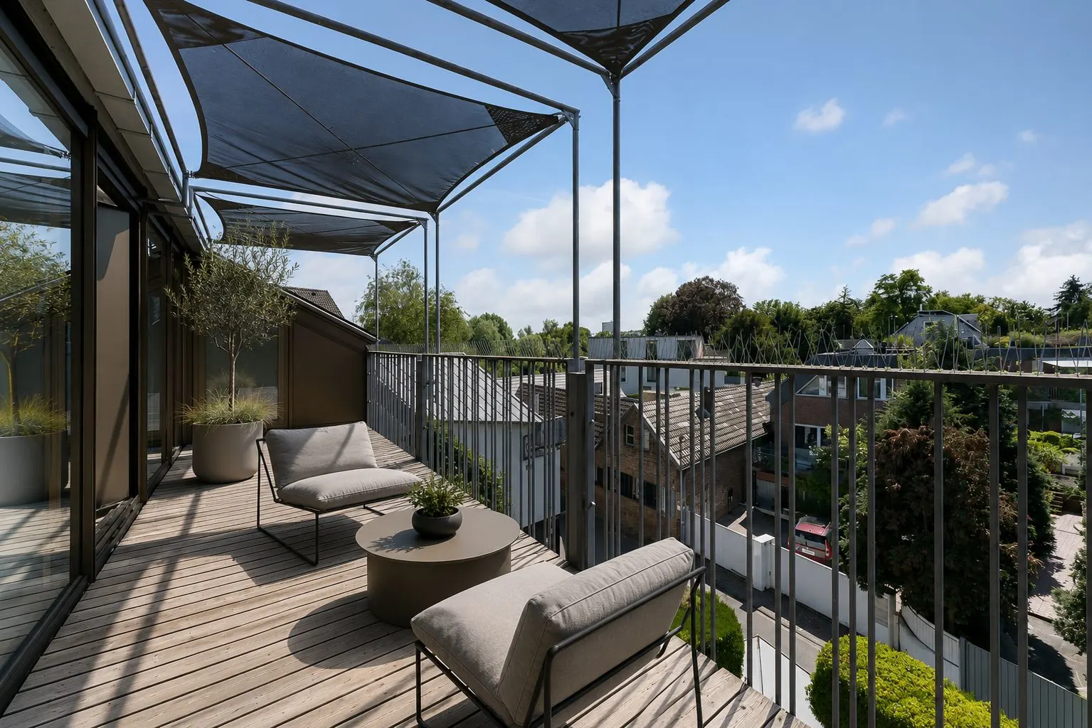 Großer Balkon mit zwei Stühlen, Tisch, Pflanzkübeln und Sonnenschutz, Blick auf Wohnhäuser.