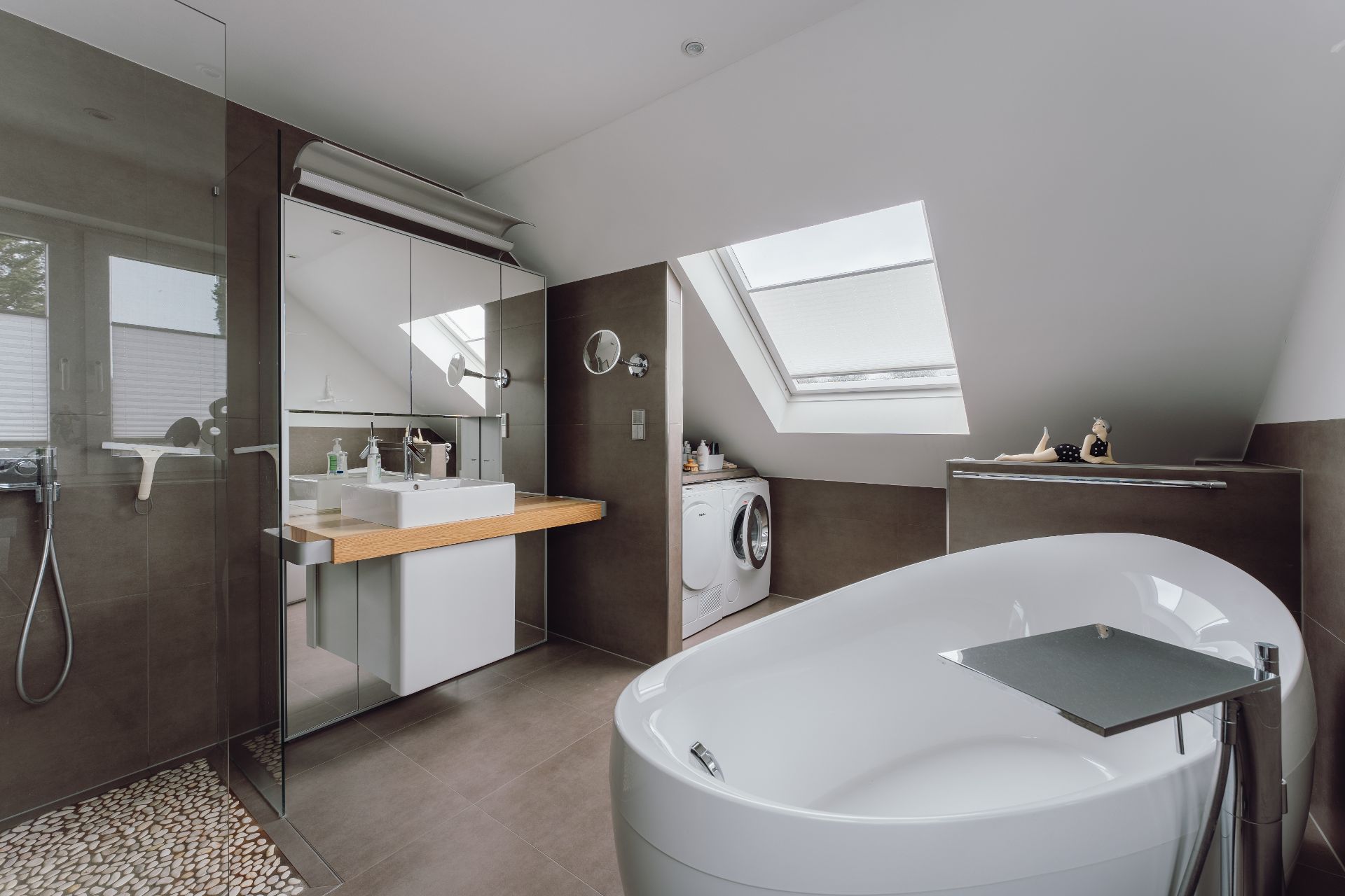 Modernes Badezimmer mit freistehender Badewanne, Dusche, Waschbecken und Waschmaschine unter Dachfenster.