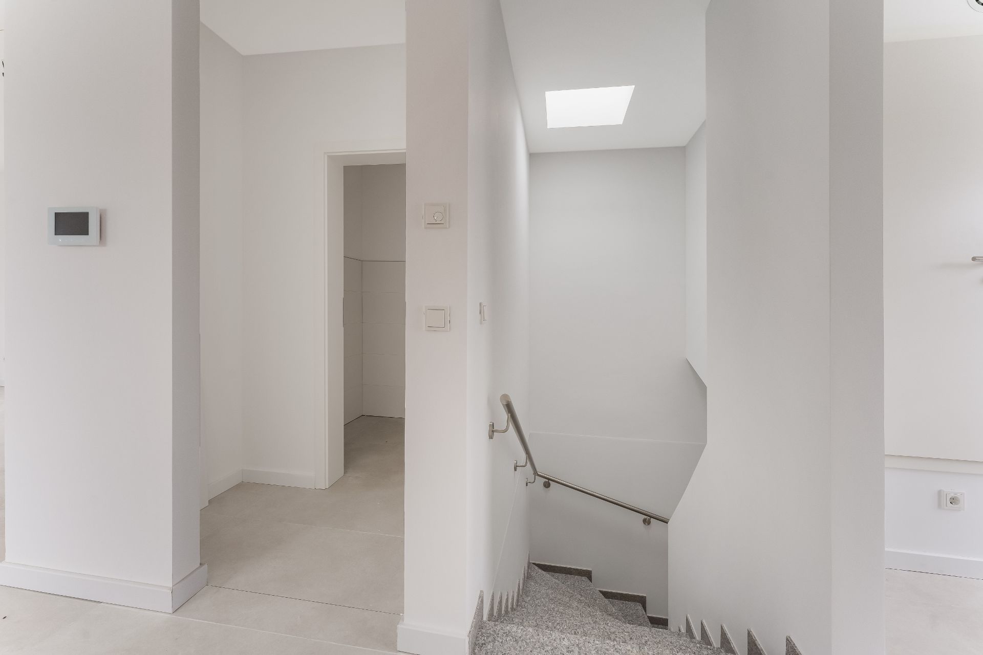 Heller Flur mit Treppenabgang, Tür zu einem weiteren Raum und Wandthermostat.