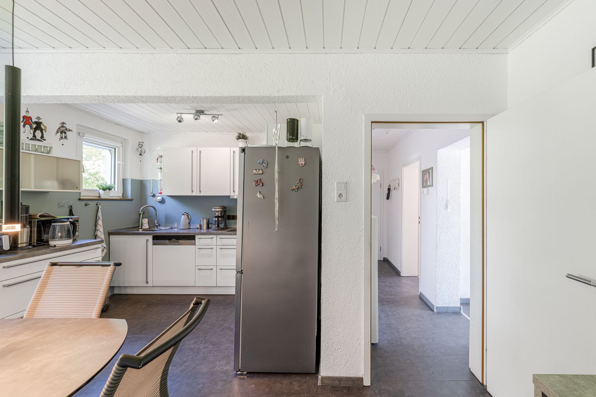 Moderne Küche mit weißen Schränken, grauem Kühlschrank und angrenzendem Flur.