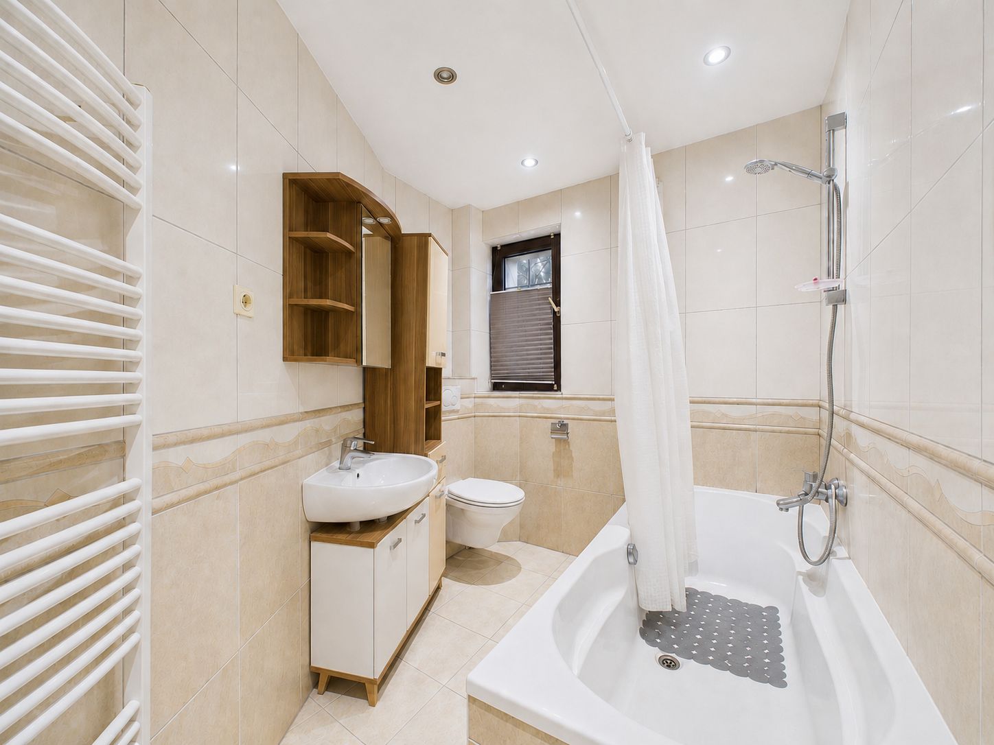Modernes Badezimmer mit Badewanne, Waschbecken, Spiegel, WC, Handtuchheizkörper und Fenster.