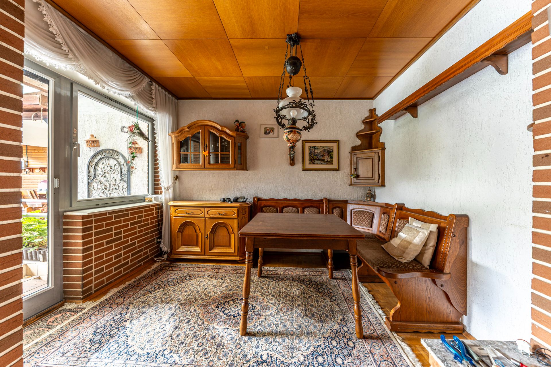 Esszimmer mit Holztisch, Eckbank, Teppich und Schrank, großes Fenster zur Terrasse.