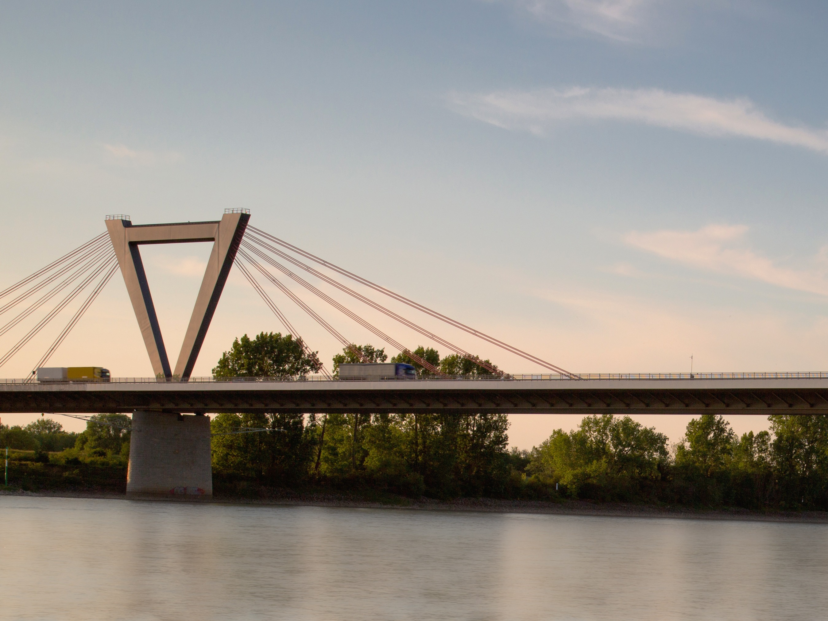 Eine moderne Schrägseilbrücke über einen Fluss, im Hintergrund Bäume und Himmel.