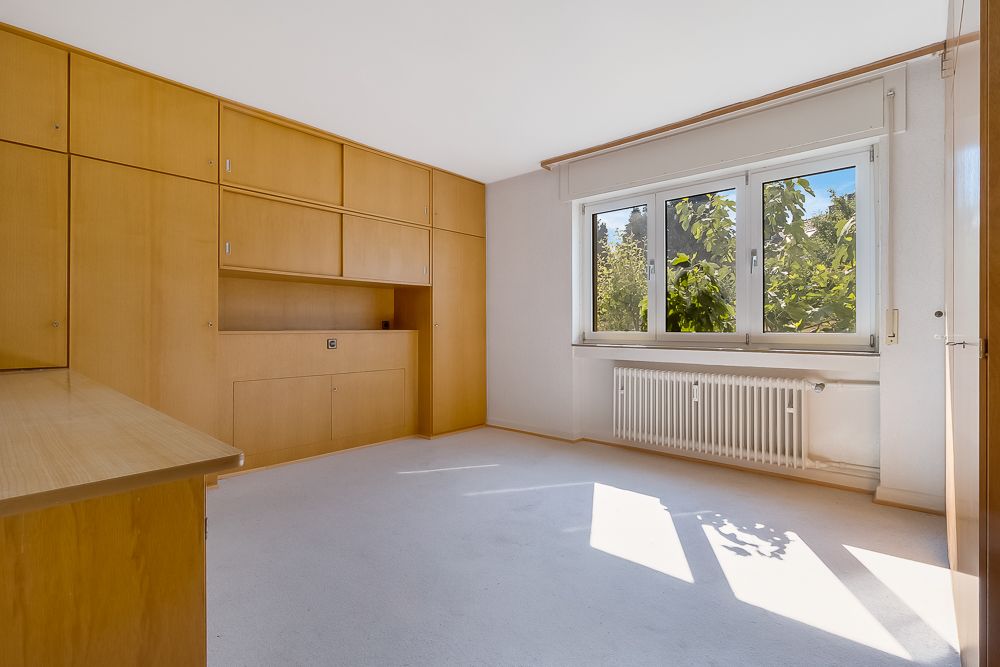 Heller Raum mit großen Fenstern, Einbauschränken aus Holz und einem Heizkörper unter dem Fenster.