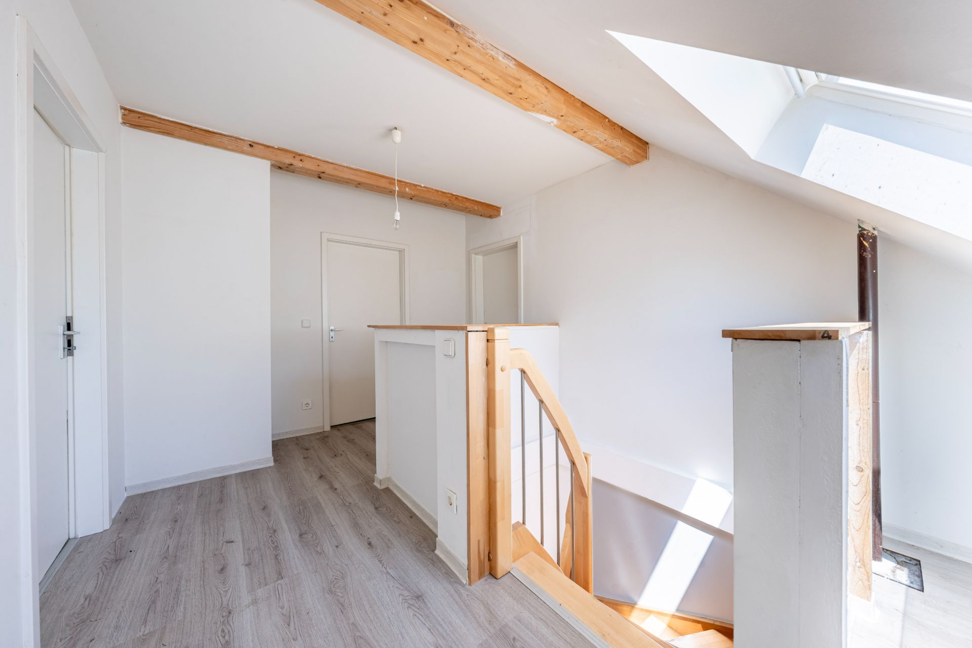 Heller Flur mit Holzgeländer, sichtbaren Deckenbalken und Dachfenster in einem Wohnhaus.
