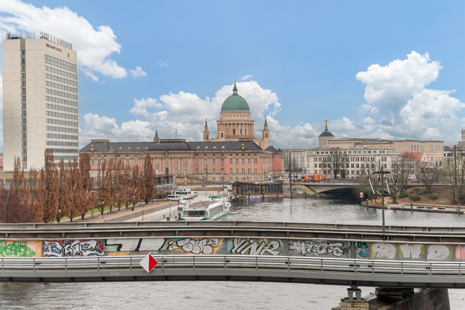 Blick auf eine Brücke mit Graffiti, Fluss und ein großes Gebäude mit Kuppel im Hintergrund.