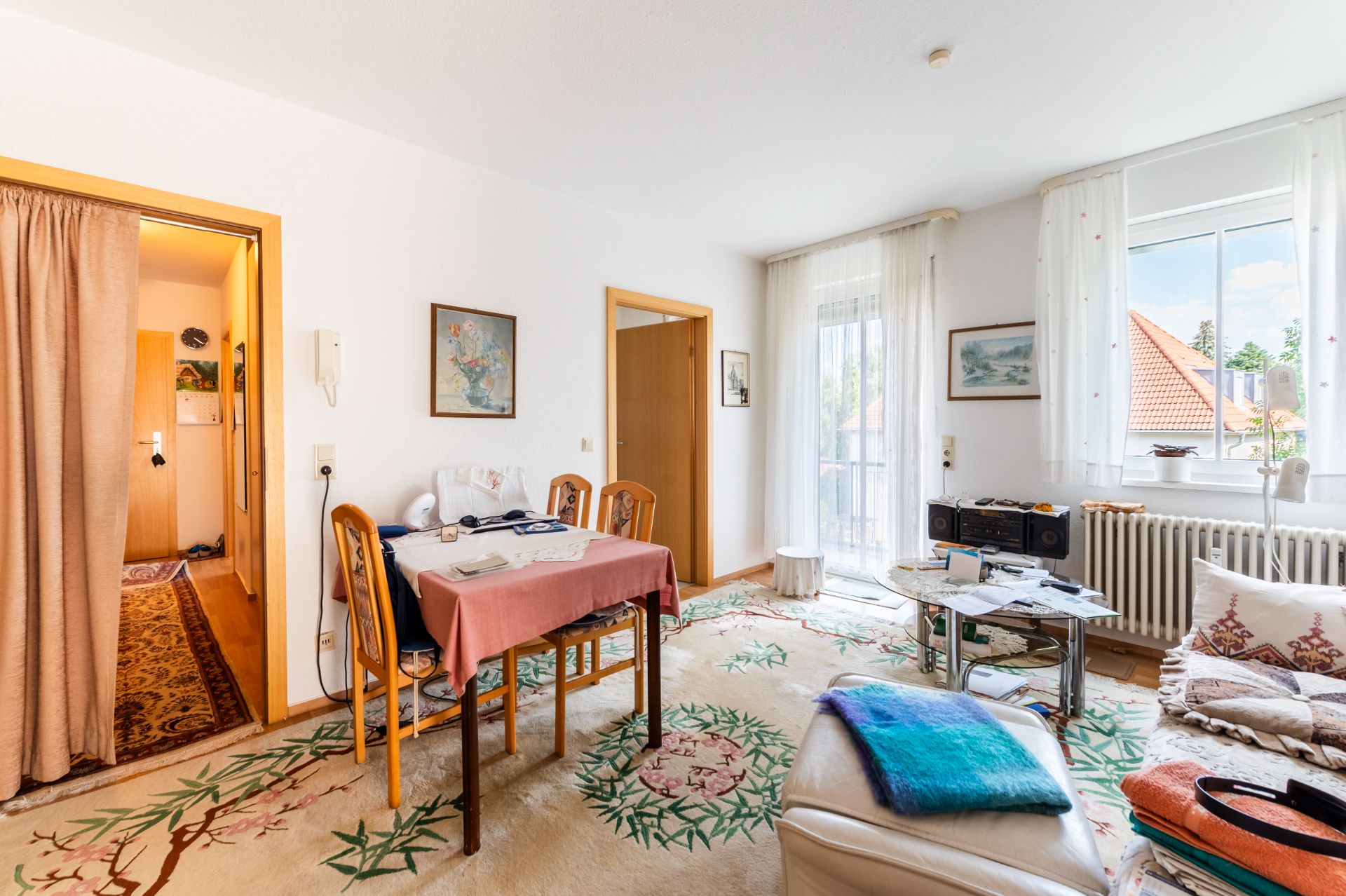 Helles Wohnzimmer mit Esstisch, Stühlen, Teppich, Sofa, Fenster und Zugang zum Balkon.