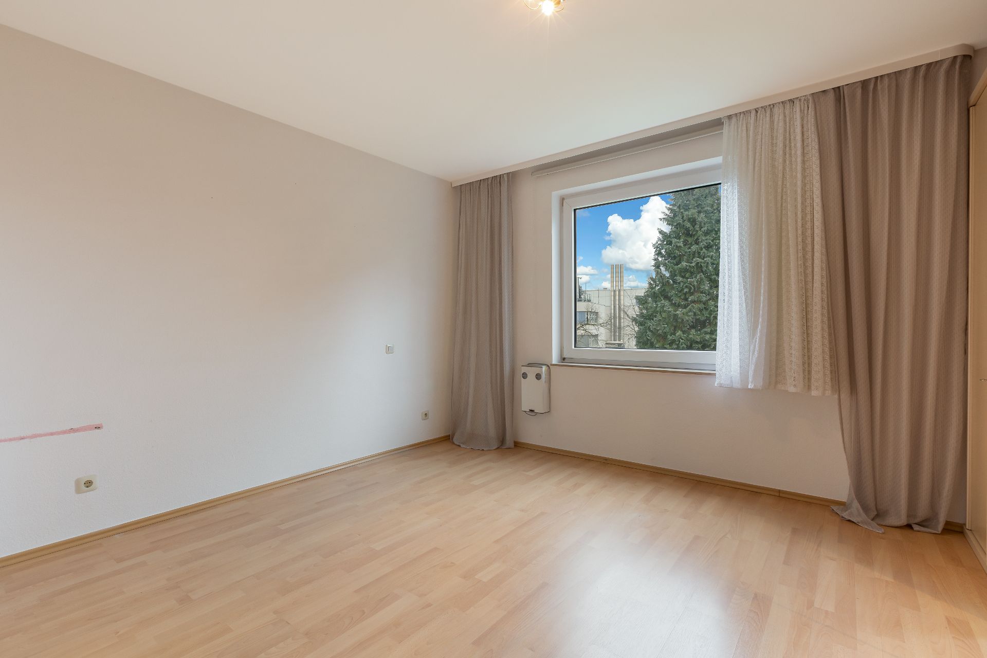 Leerer Raum mit Holzfußboden, Fenster mit Vorhängen und Blick nach draußen.