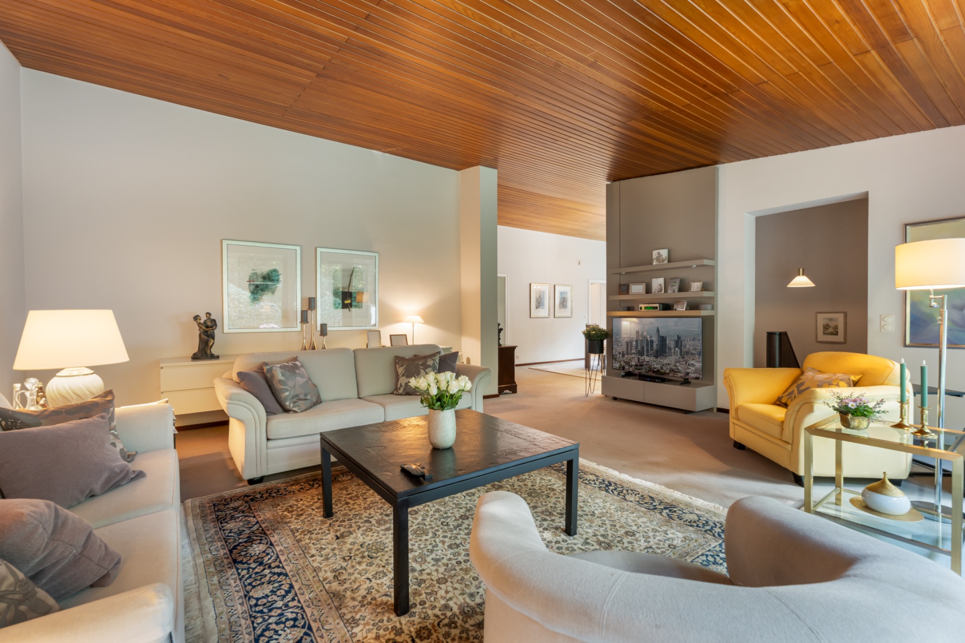Helles Wohnzimmer mit Sofa, Sesseln, Holzboden und Teppich, dekoriert mit Lampen und Bildern.