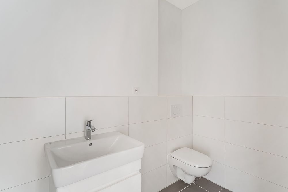 Helles Bad mit weißem Waschbecken, Wand-WC und weißen Fliesen.