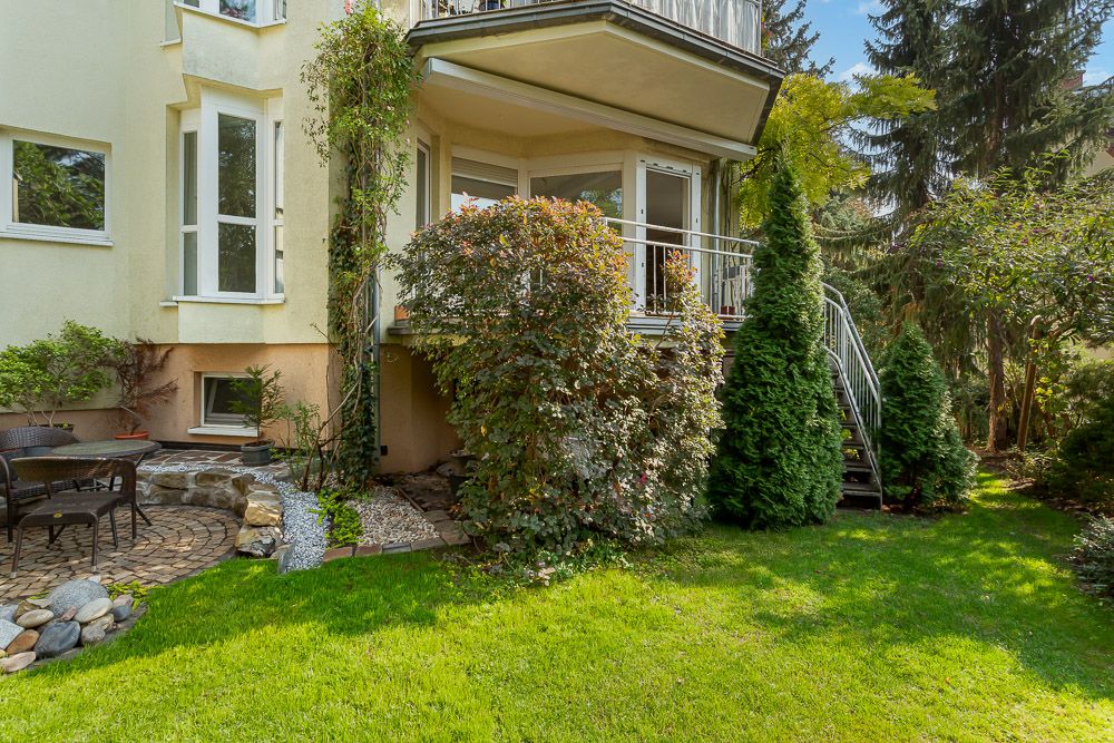 Grüner Garten mit Terrasse, Sitzbereich und Außentreppe an einem Wohnhaus.