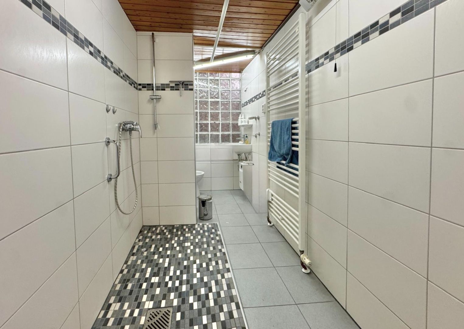 Modernes, barrierefreies Badezimmer mit bodengleicher Dusche, weißen Fliesen und Holzdecke.