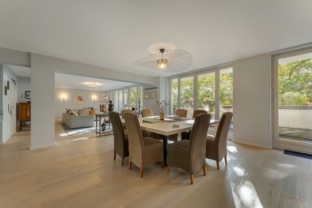 Helles Esszimmer mit großem Tisch, acht Stühlen und Glasfront zu Balkon, verbunden mit Wohnzimmer.