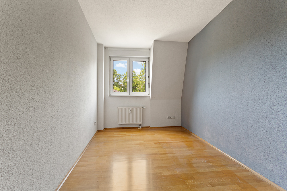 Leerer Raum mit Holzboden, grauen Wänden und Fenster mit Blick ins Grüne.
