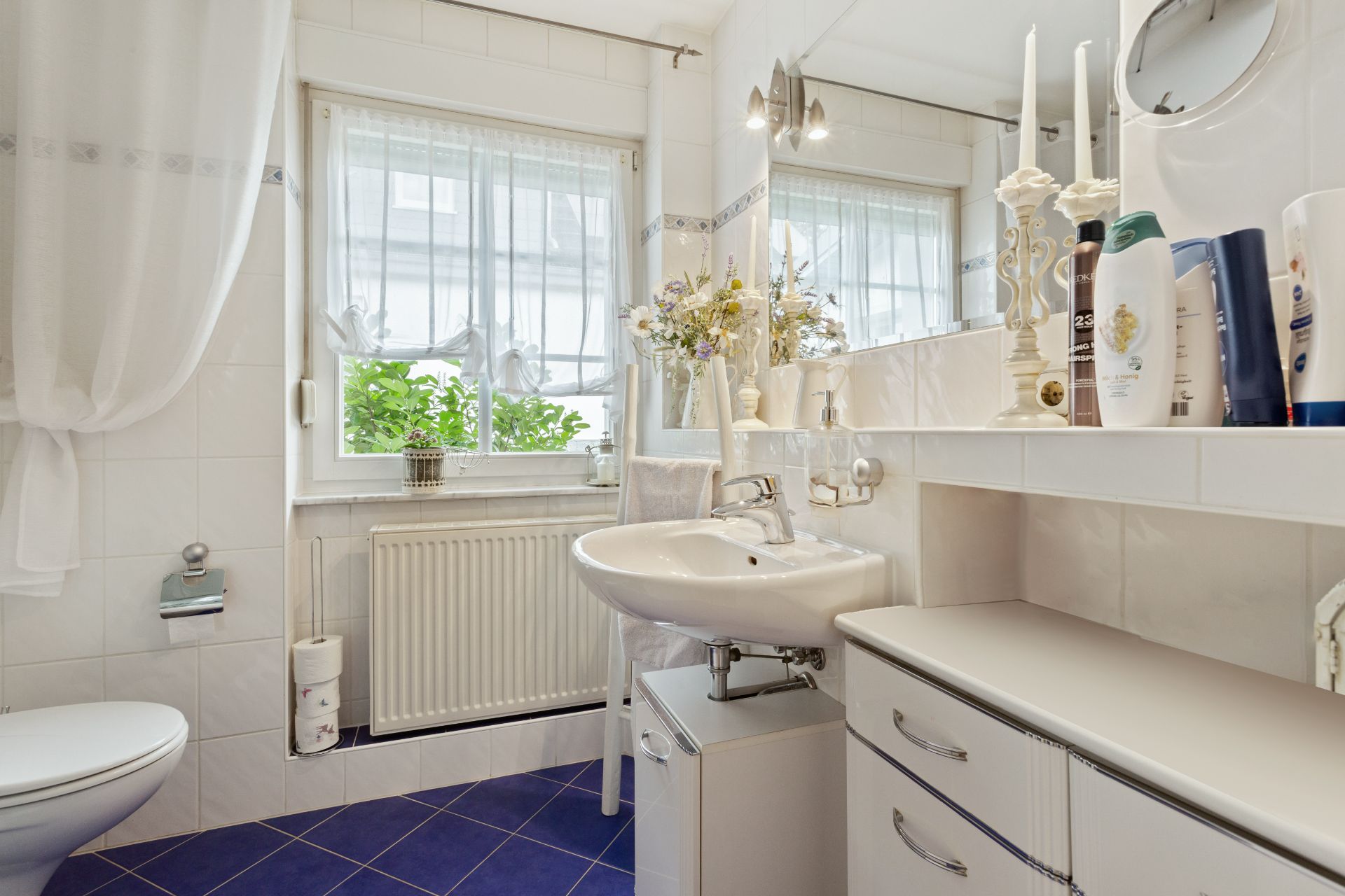 Helles Badezimmer mit großem Fenster, Waschbecken, Toilette und blauen Fliesen.