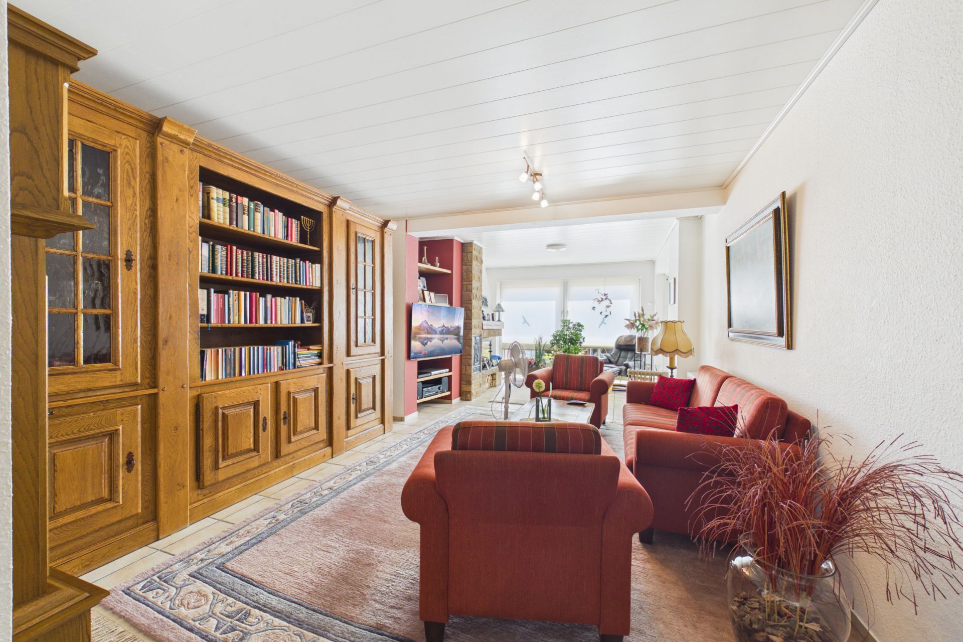 Helles Wohnzimmer mit roten Sofas, großem Bücherregal, Fernseher und Teppich.
