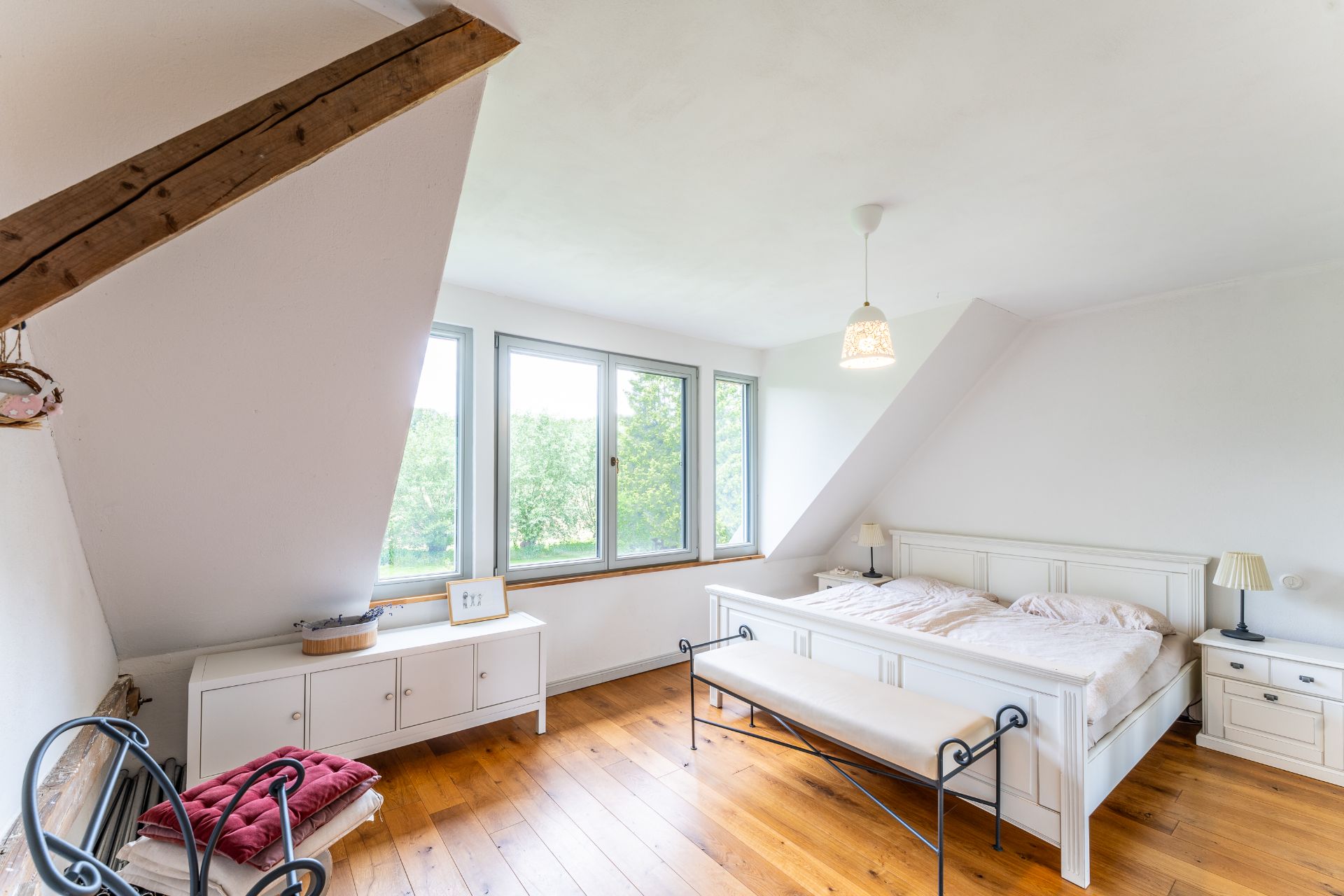 Helles Schlafzimmer mit Holzboden, Doppelbett, Bank und großen Fenstern.