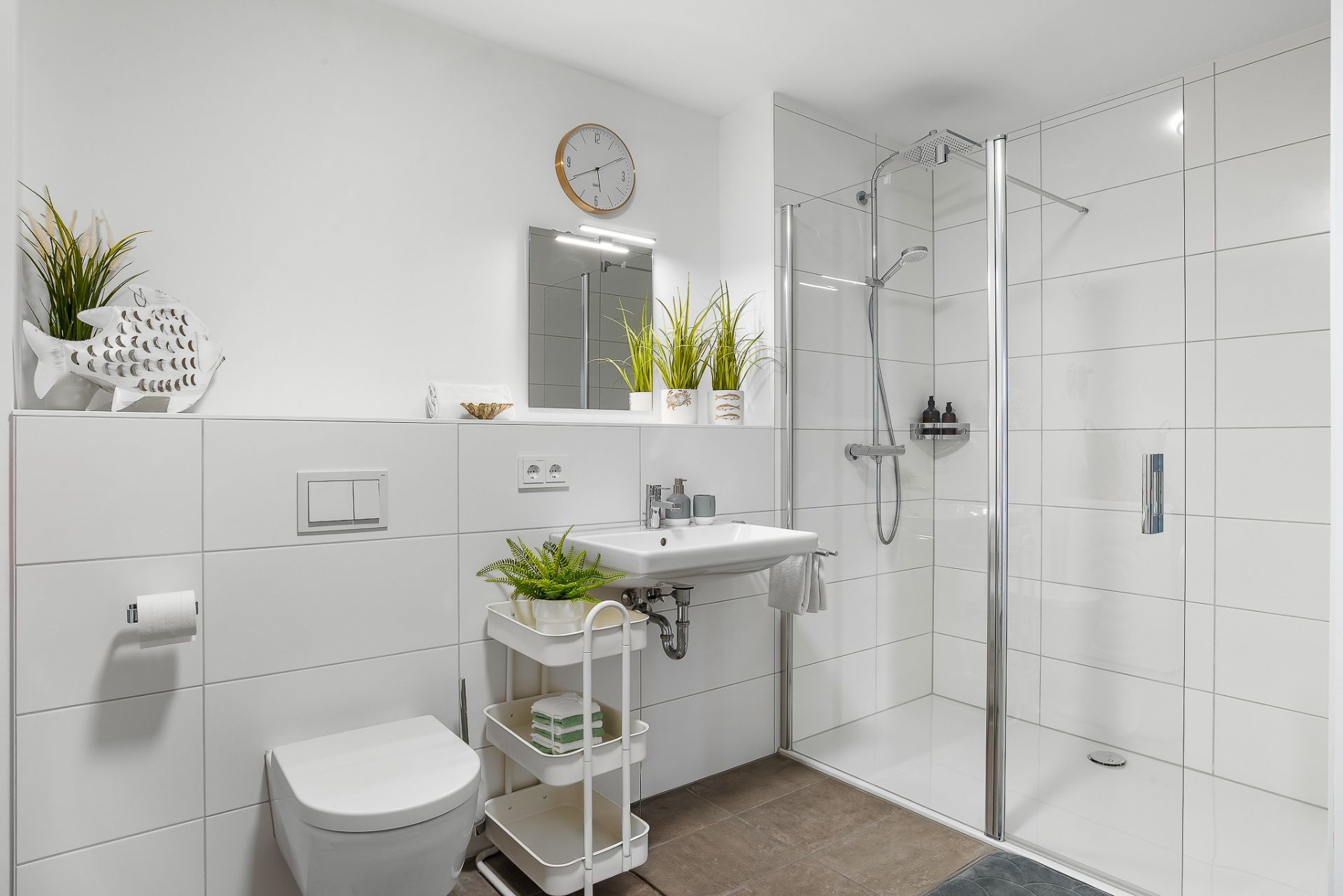 Modernes Bad mit Dusche, Toilette, Waschbecken und Pflanzen auf weißen Fliesen.