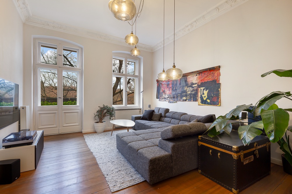 Helles Wohnzimmer mit grauem Sofa, Couchtisch, großen Fenstern und Zimmerpflanzen.