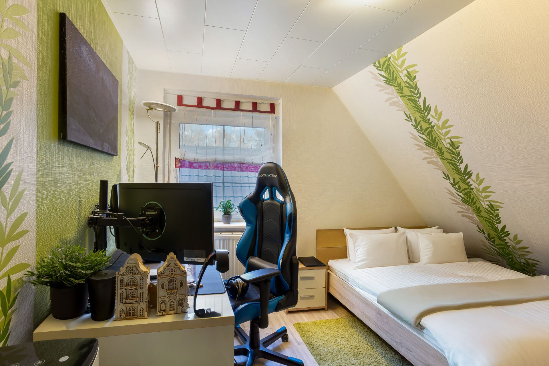 Modernes Schlafzimmer mit Schreibtisch, Monitor, Bürostuhl und Einzelbett unter Dachschräge.