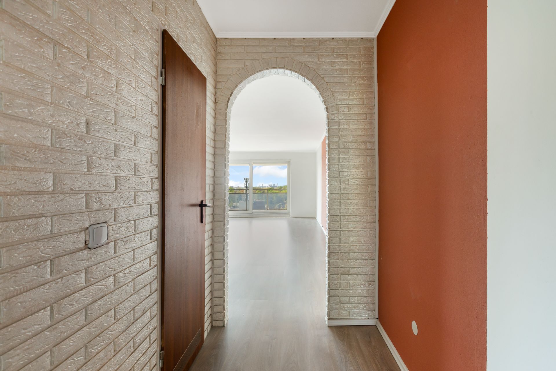 Flur mit roter Wand, Bogendurchgang und Blick ins helle Wohnzimmer mit Fenster.