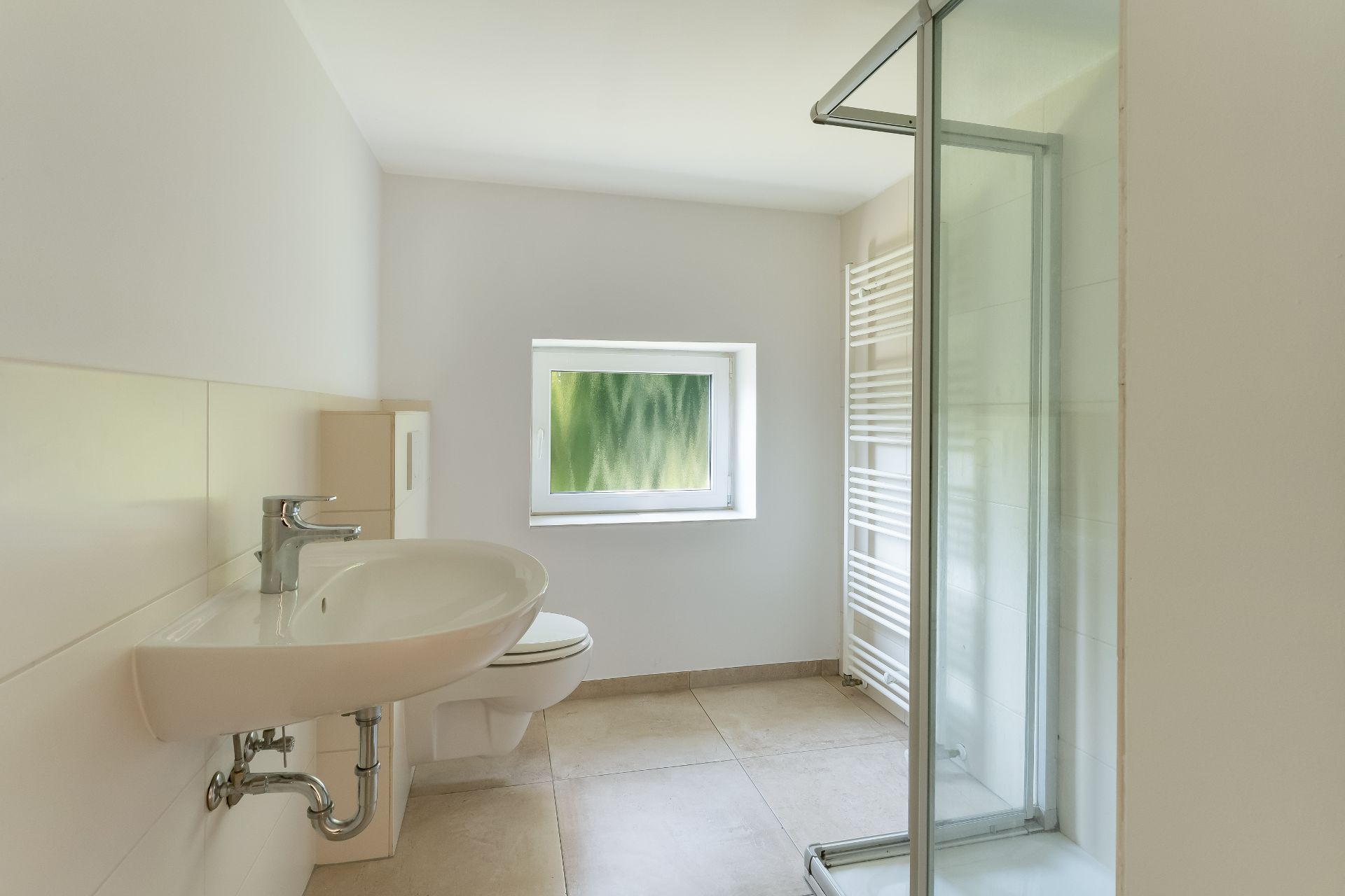 Modernes, helles Badezimmer mit Dusche, Waschbecken, WC und kleinem Fenster.