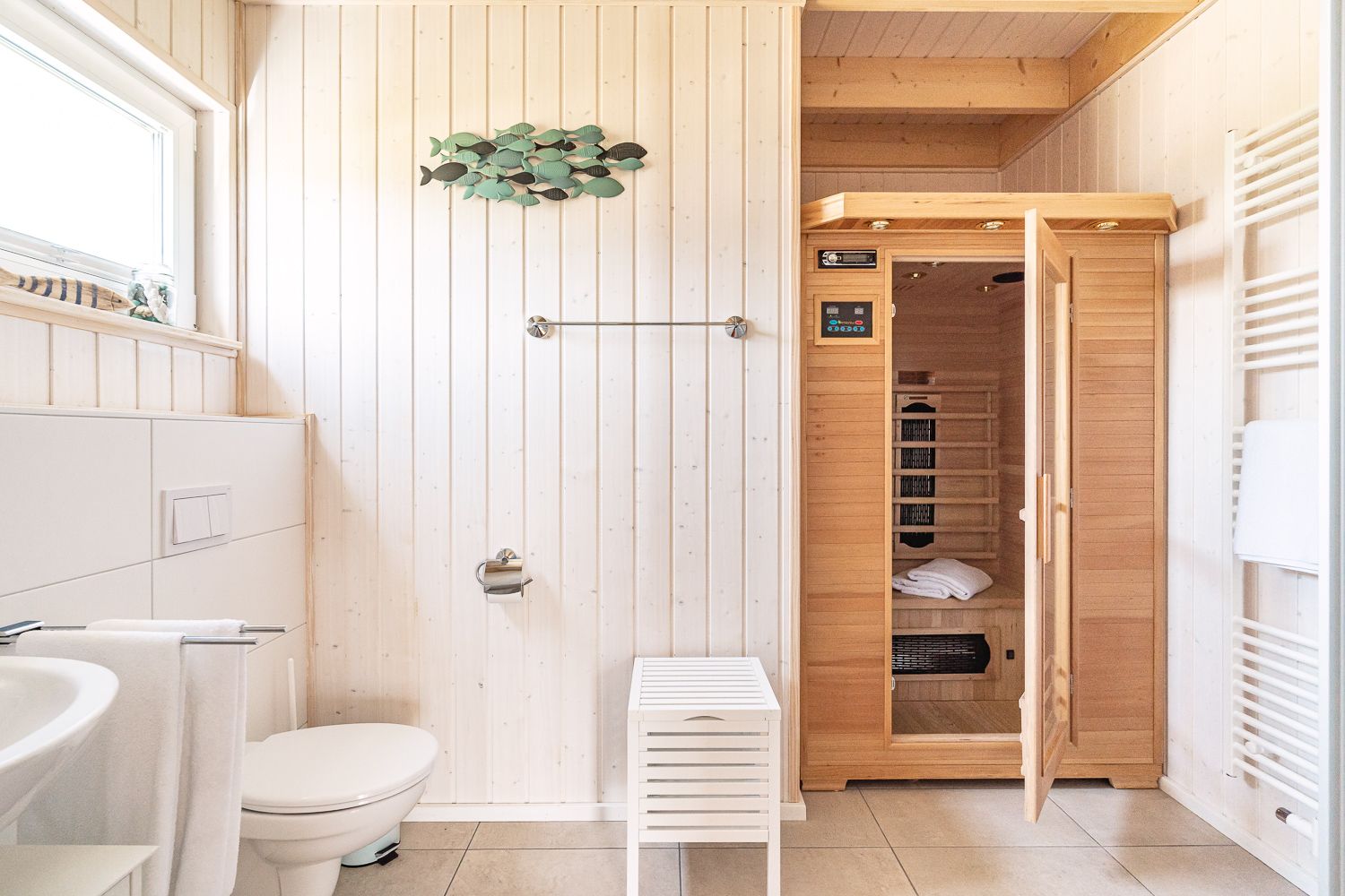 Helles Badezimmer mit Toilette, Waschbecken und offener Holzsauna.