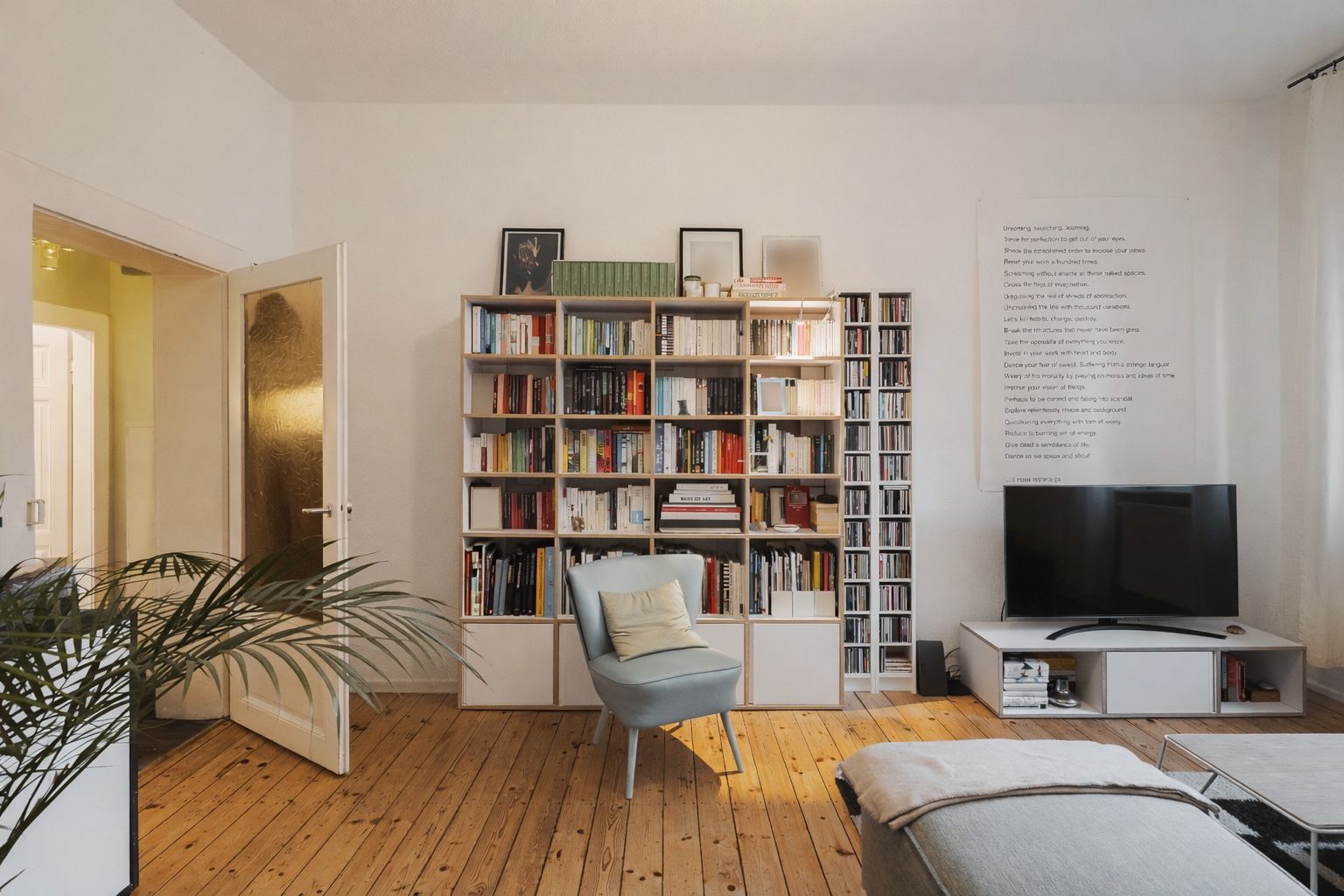 Wohnzimmer mit Bücherregal, Sessel, Fernseher auf TV-Möbel und Holzboden.