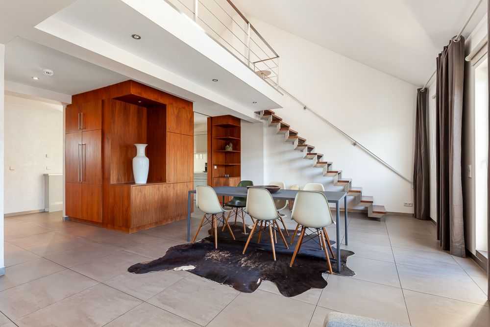 Modernes Esszimmer mit Holztisch, sechs Stühlen, Teppich und offener Treppe im Hintergrund.