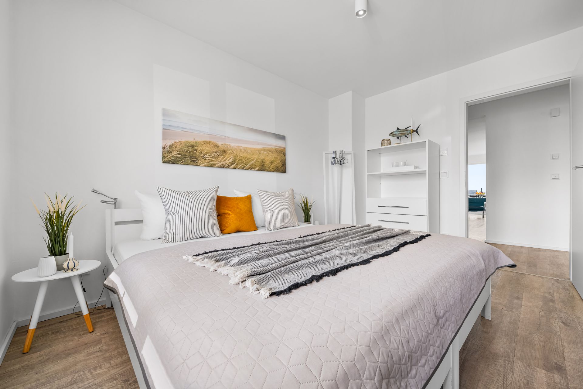 Helles Schlafzimmer mit Doppelbett, Nachttisch, Regal und Wandbild.