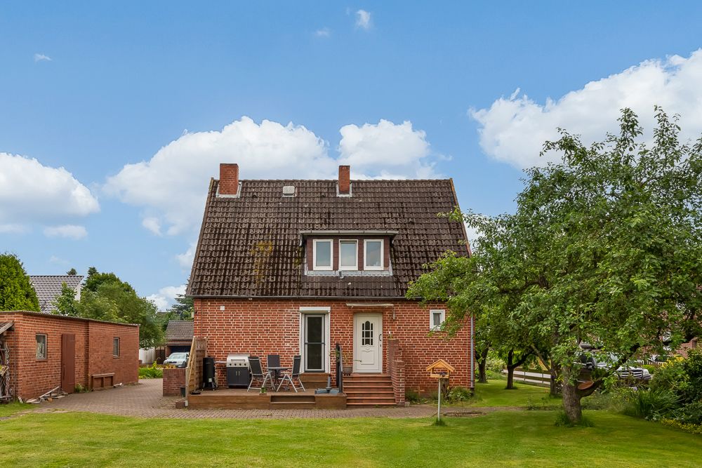 Backsteinwohnhaus mit Terrasse, Sitzgruppe und Garten, Baum im Vordergrund.