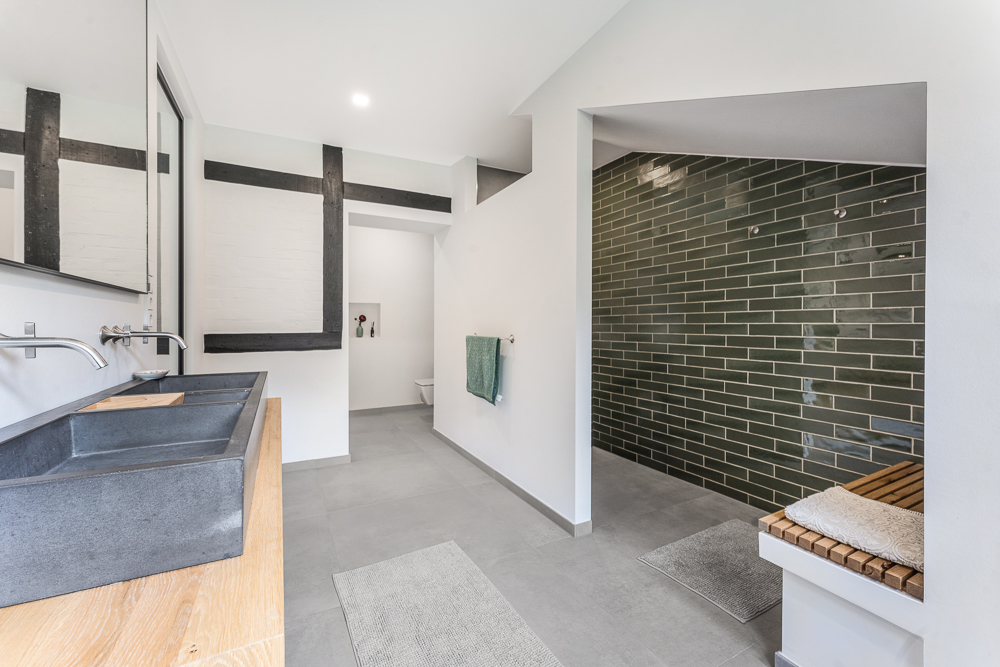 Modernes Badezimmer mit Doppelwaschbecken, großer Dusche und grüner Fliesenwand.