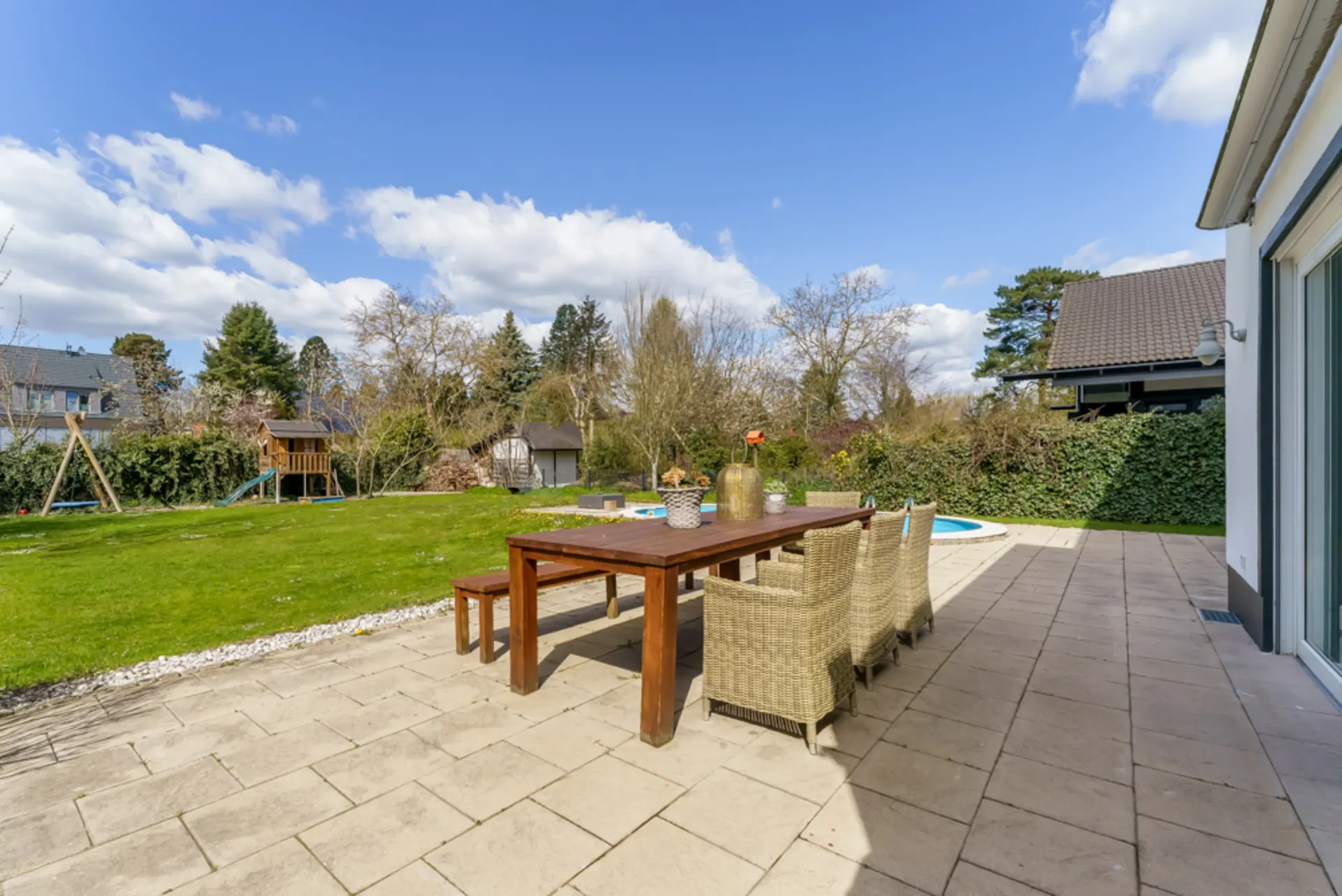 Terrasse mit großem Holztisch, Stühlen und Blick auf Garten mit Spielplatz.