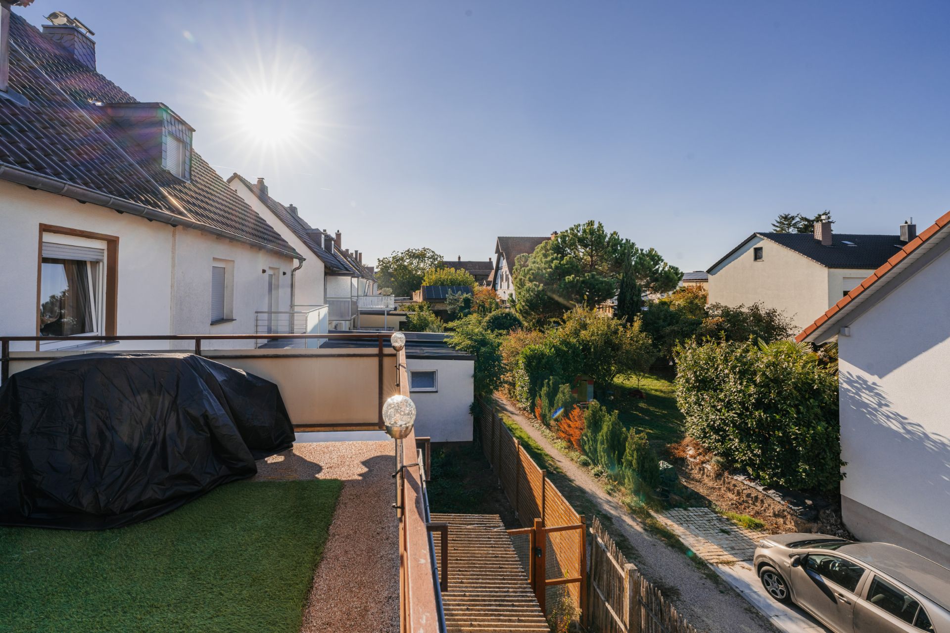 Blick von einem Balkon auf einen Garten und Nachbarhäuser bei Sonnenschein.