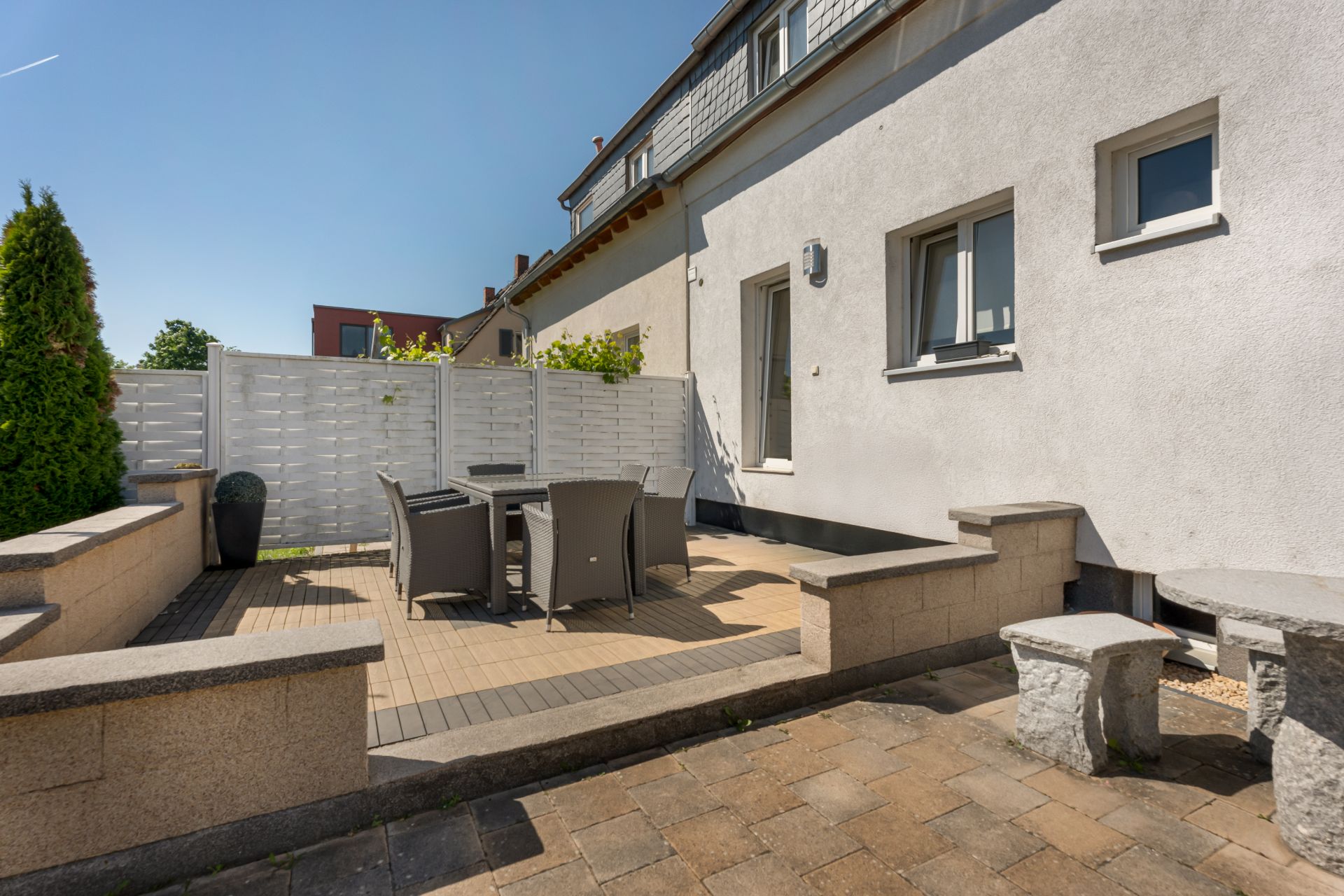 Moderne Terrasse mit Tisch, vier Stühlen und Steinbank neben einem Wohnhaus.