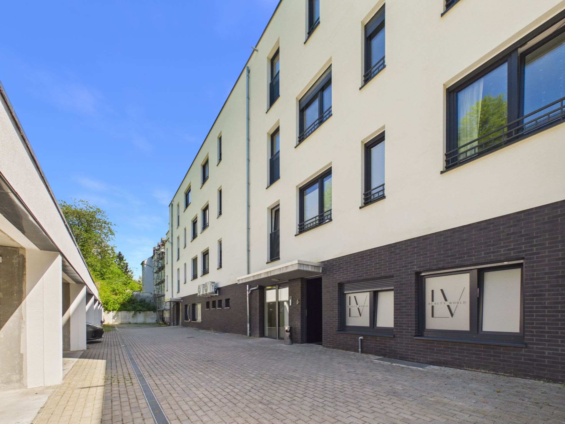 Moderner Wohnhaus-Eingang mit mehreren Fenstern und gepflastertem Vorplatz.