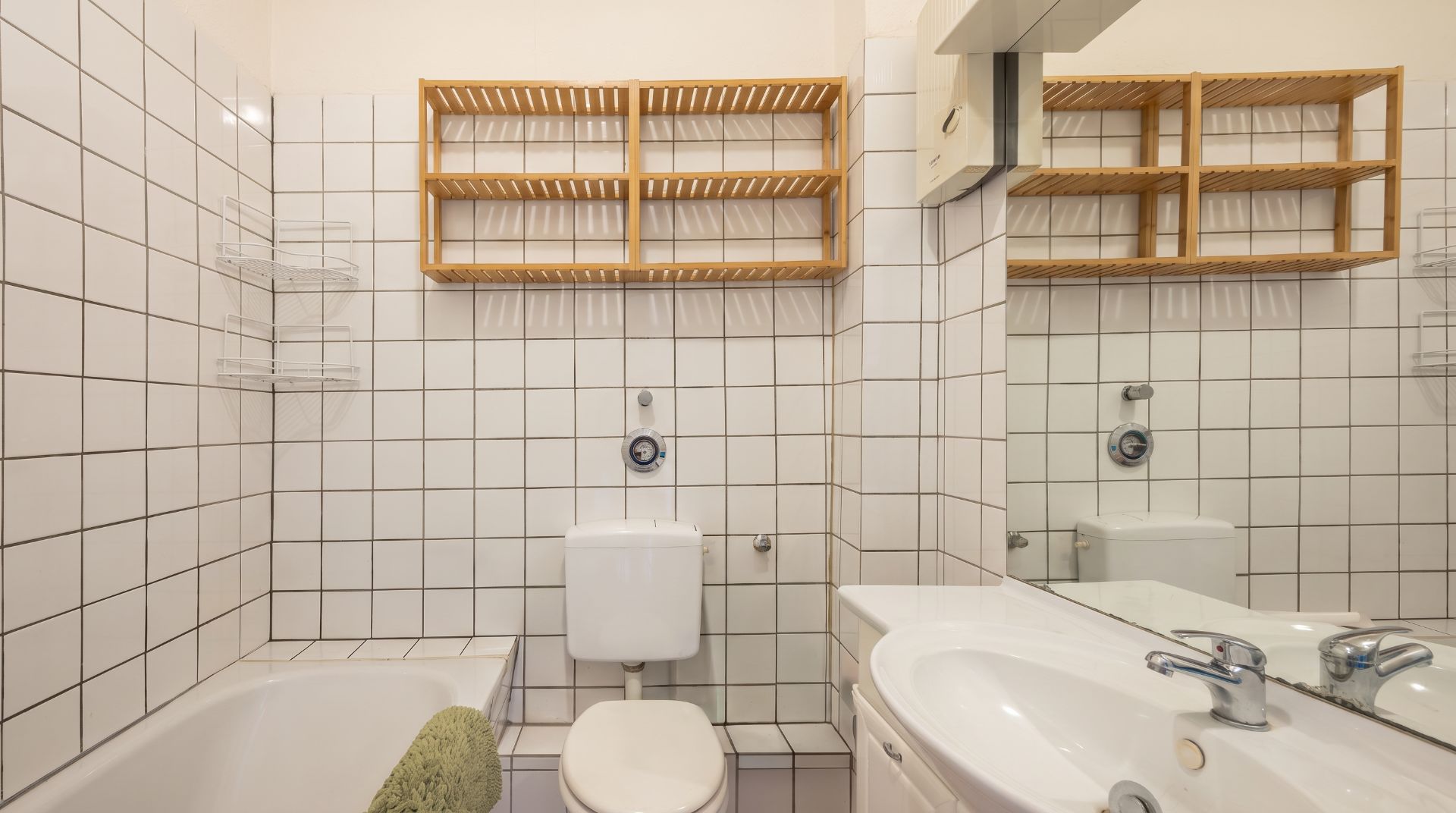 Helles Badezimmer mit Badewanne, Toilette, Waschbecken und Holzregalen an der Wand.