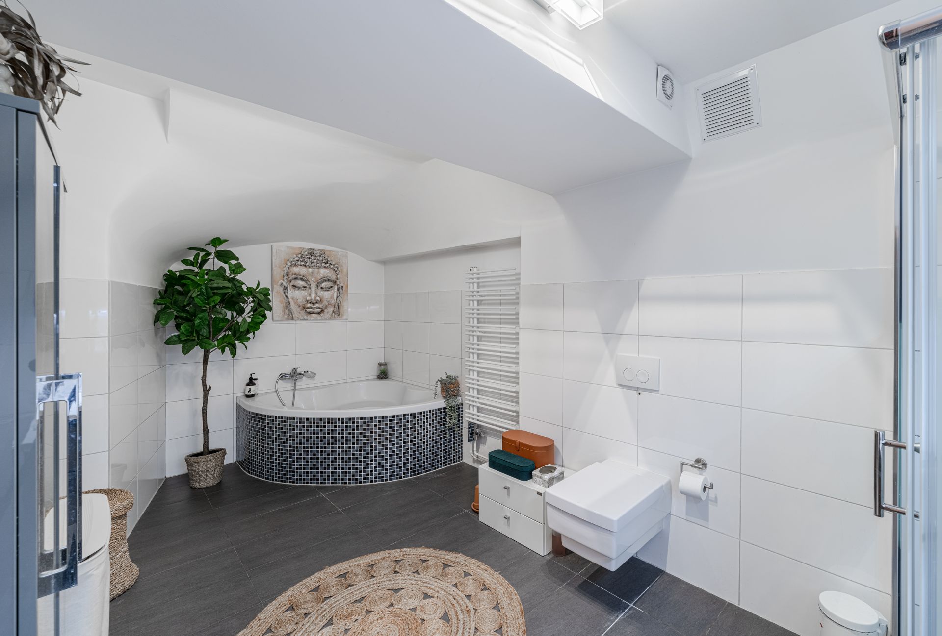 Modernes Badezimmer mit Eckbadewanne, großem Bild, Pflanze und Wandtoilette.
