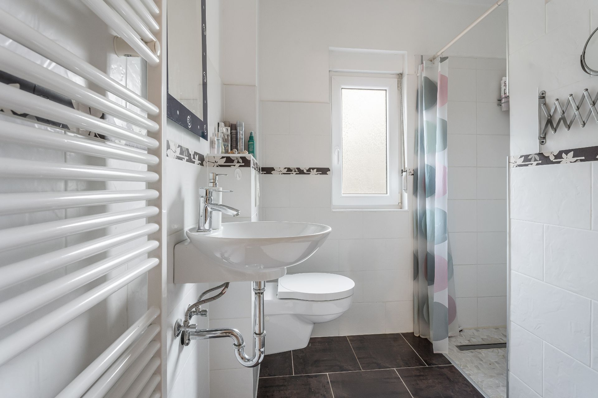 Modernes Badezimmer mit Waschbecken, Wandspiegel, Toilette, Dusche und Handtuchheizkörper.